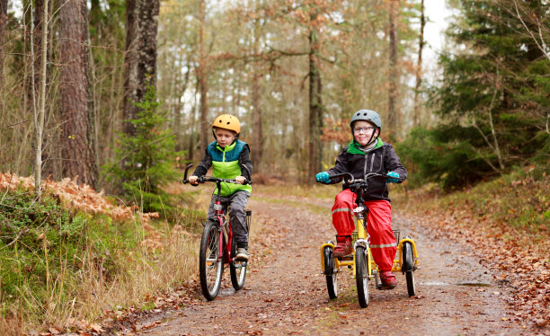 Två barn i regnkläder som cyklar på en grusväg.