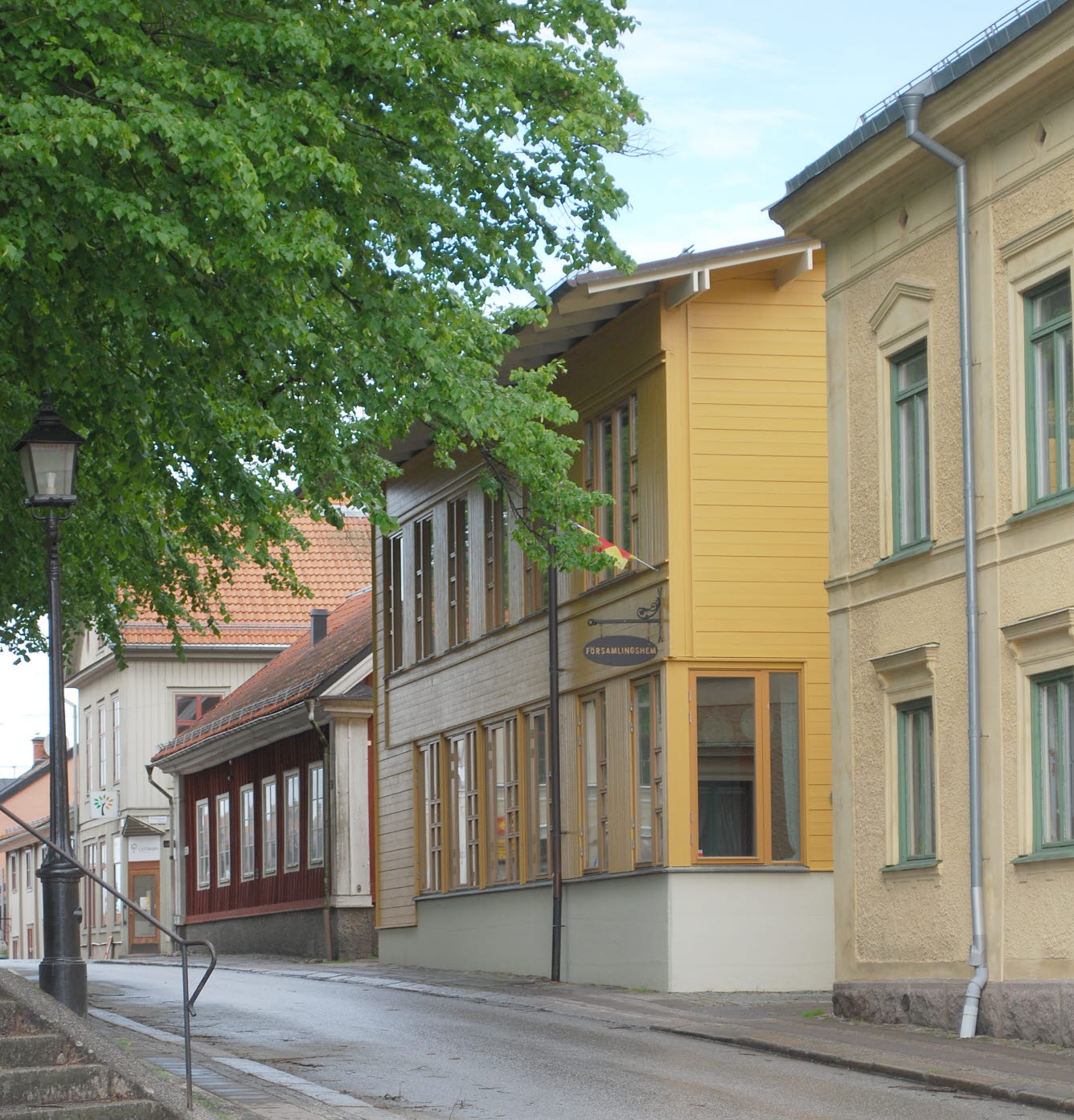 En gul träbyggnad i två våningar vid en trottoar.