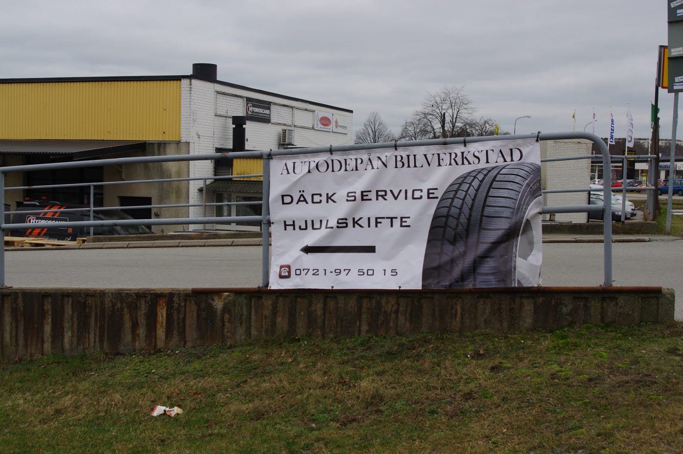 Foto på en banderoll med reklam för däckservicevid uppsatt på ett staket vid en bilverkstad.