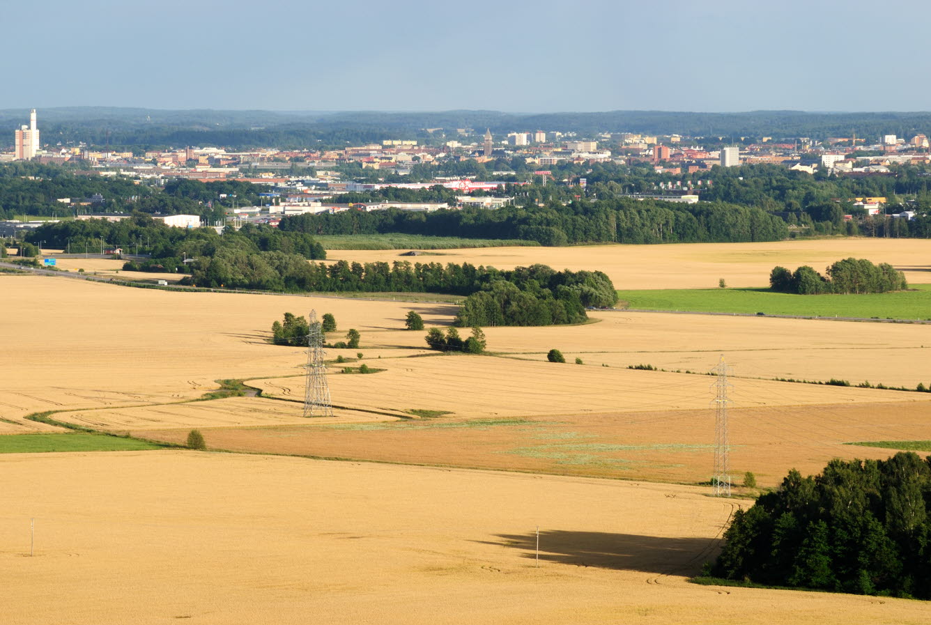 Flygfoto av landskap med stora sädesfält och en tätort med bostäder, handelsområde och industri. 