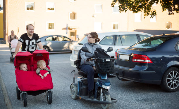 Person i permobil på promenad tillsammans med annan person som kör en röd tvillingvagn.