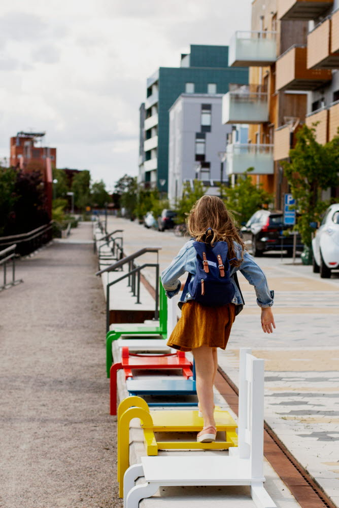 Flicka som hoppar på färgglada stolar längs med ett gångstråk i ett bostadsområde.
