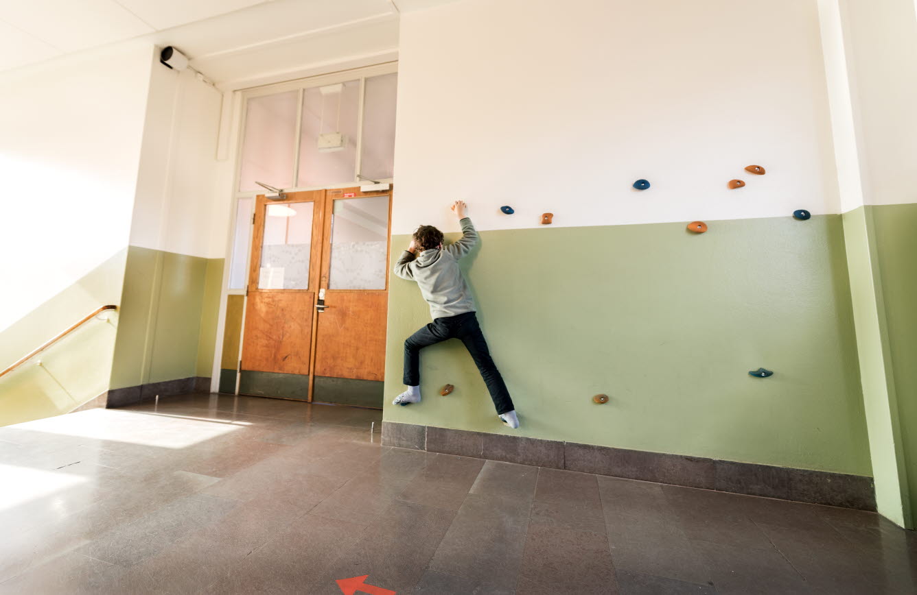 Korridor med ett barn som klättrar på de uppsatta fot- och handstegen som finns på väggen.