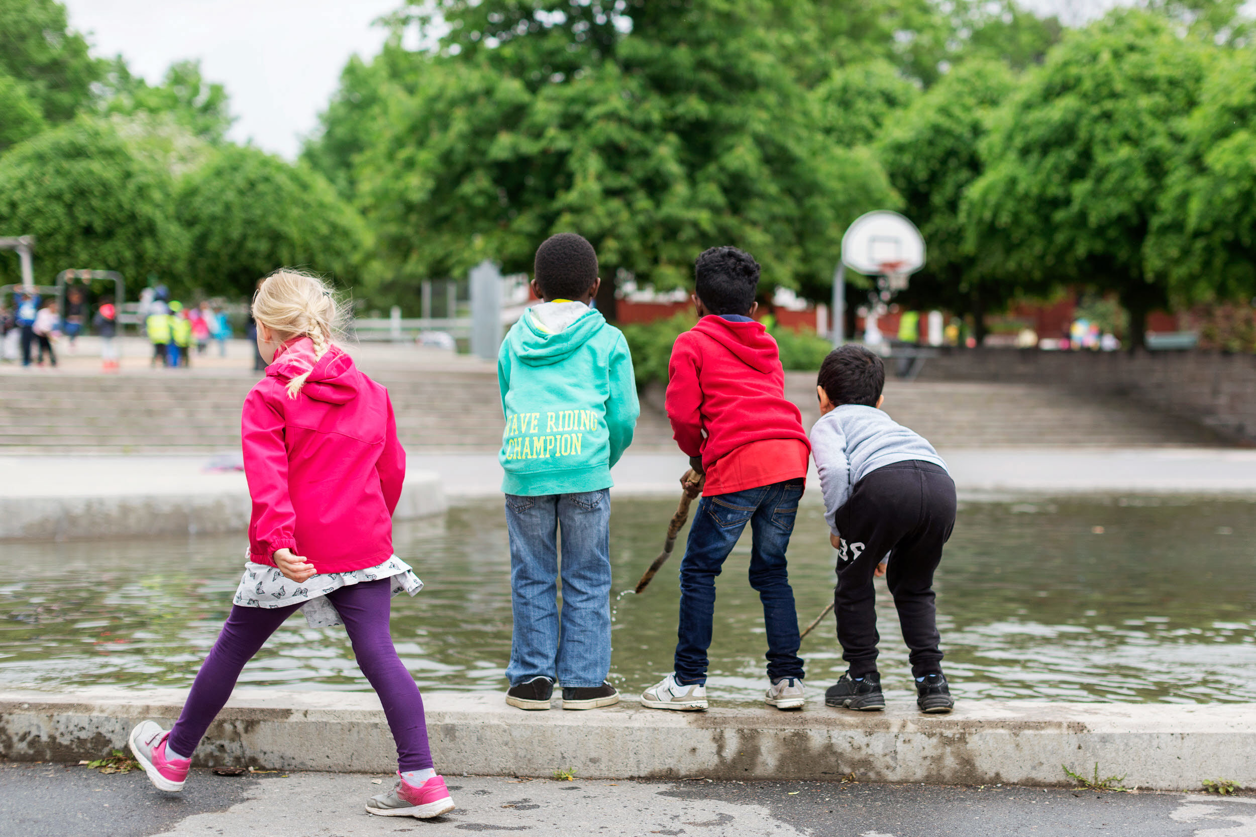 Foto med fyra barn som leker vid en damm i en park.