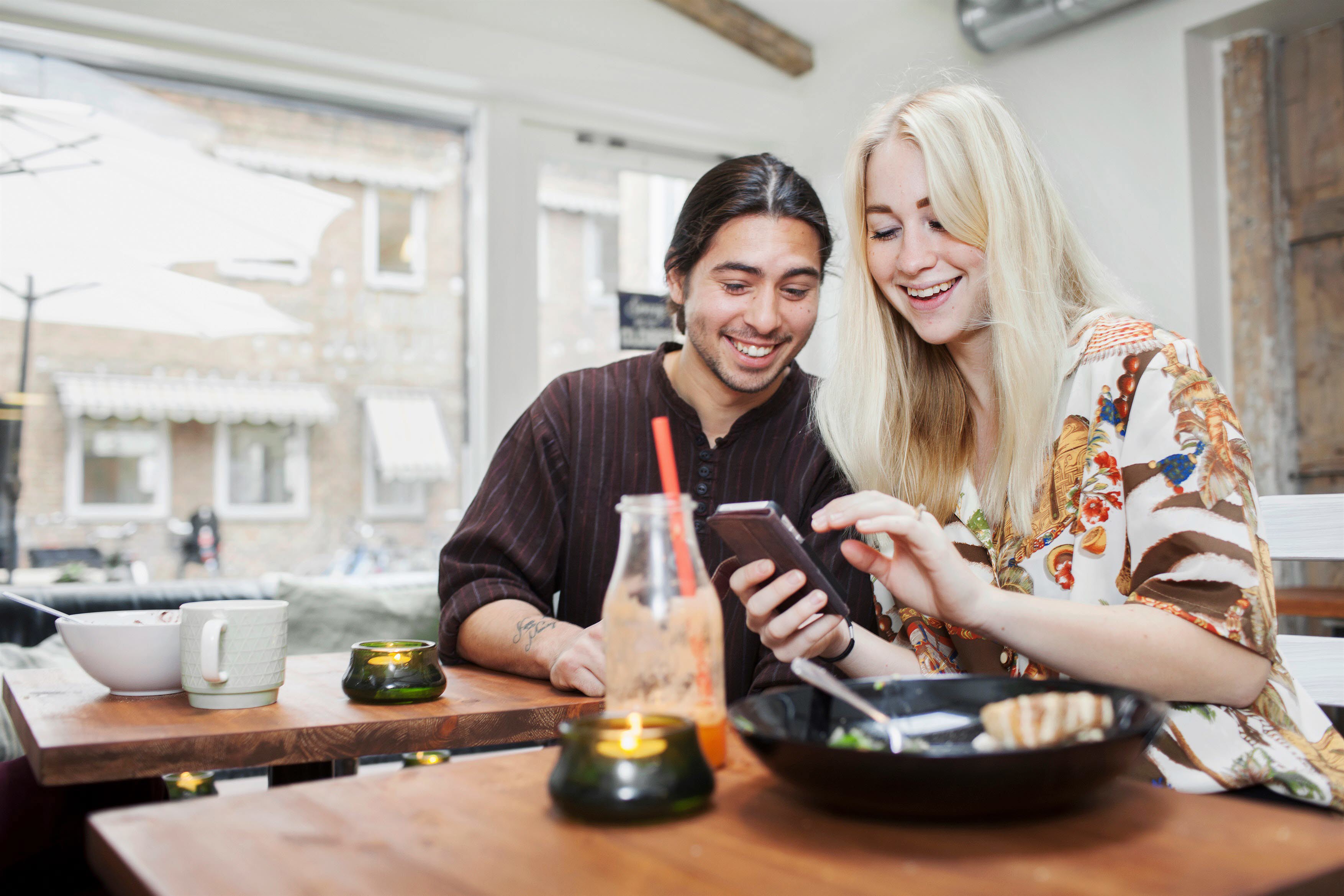 Två ungdomar umgås på café och tittar på en smartphone.