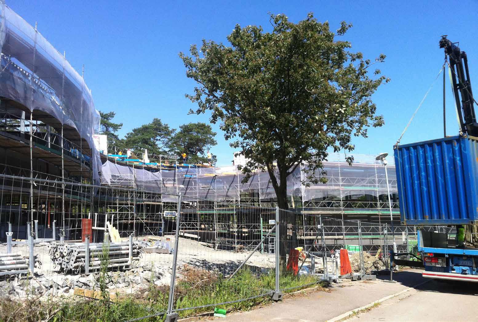 Foto som visar en byggarbetsplats när en blå container lyfts av ett lastbilsflak.