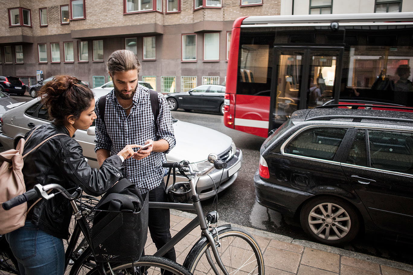 Bild på ungt par med cyklar i stadsmiljö som söker information i sina telefoner. 