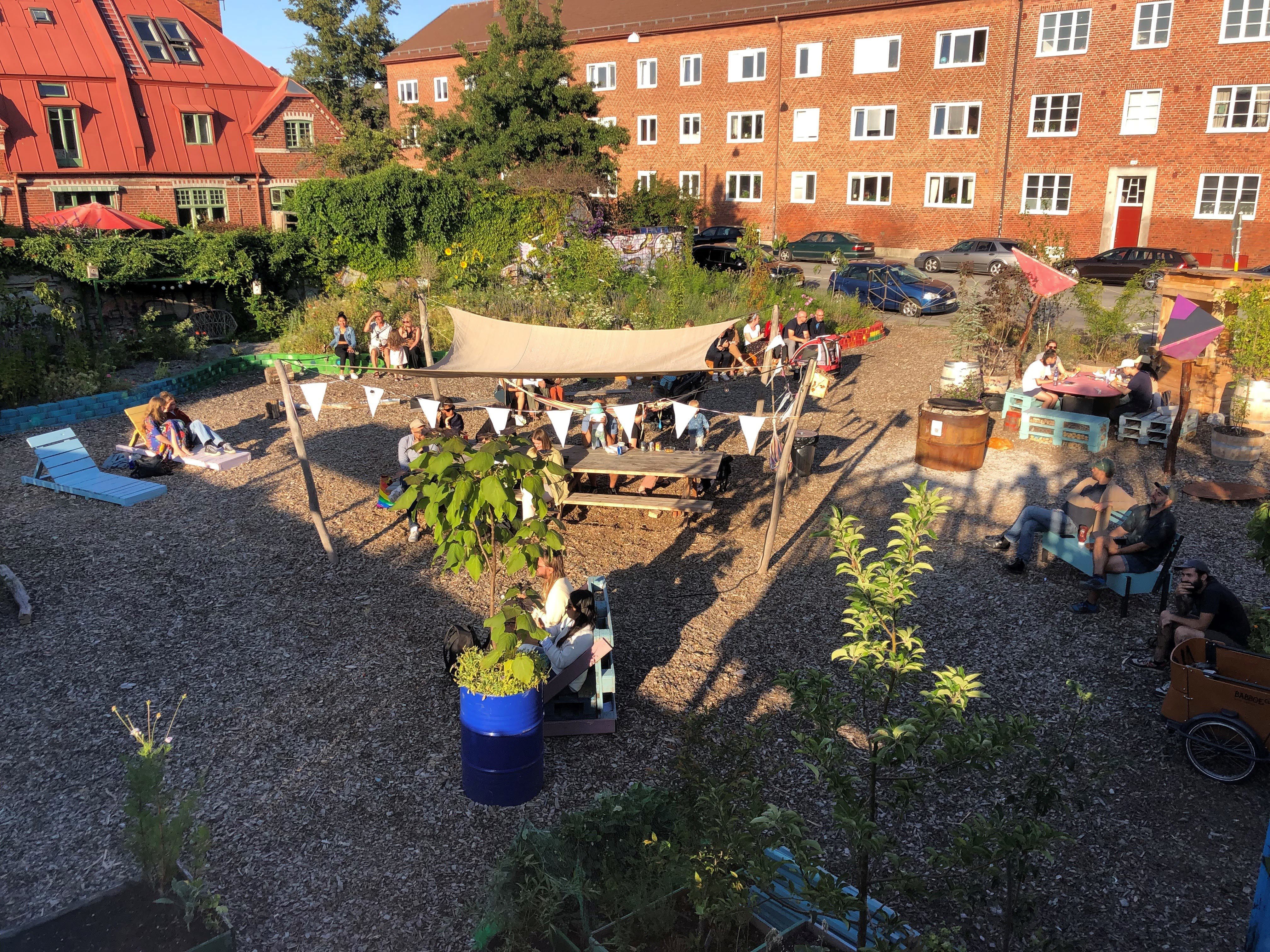 Foto som visar en innergård vid flerbostadshus med växter, solstolar och soltak. 