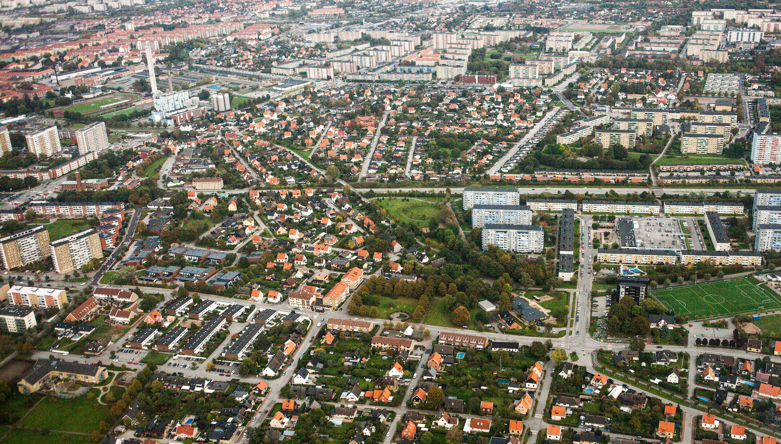 Flygfoto över en stad med tydliga stadsdelar, vägar och gröna områden.