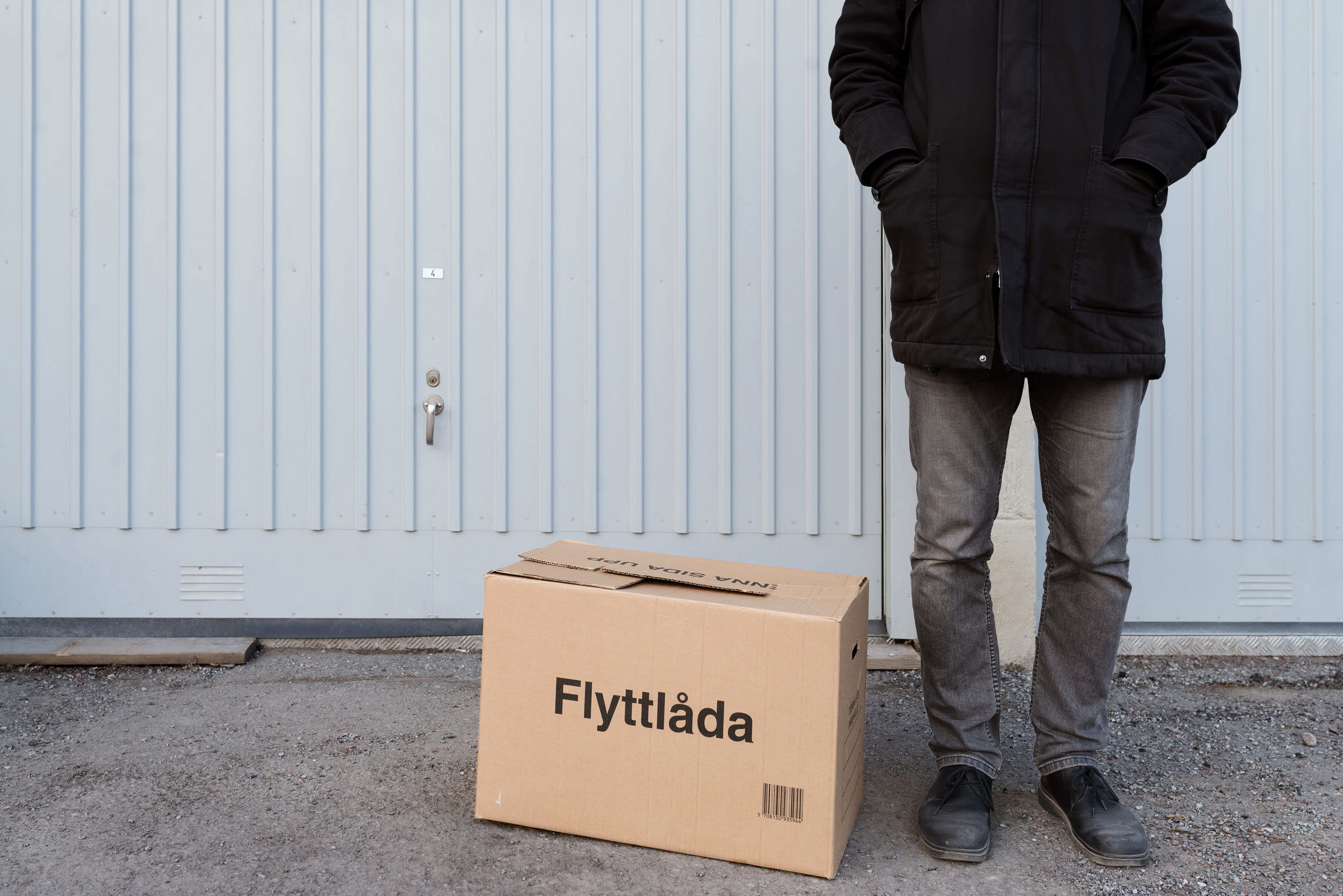 Person som står utanför ett garage, bredvid en flyttkartong.