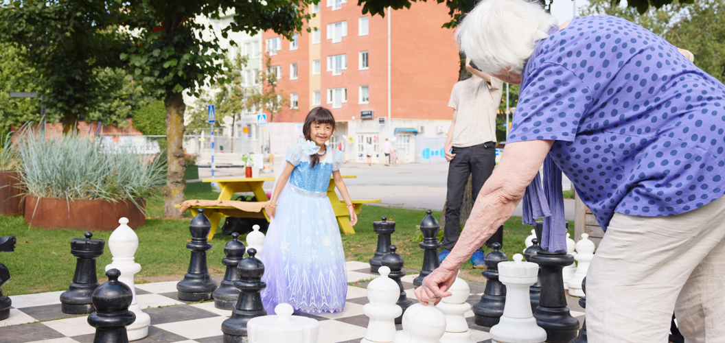 Människor umgås utomhus över generationsgränserna, vid ett schackspel i en park.