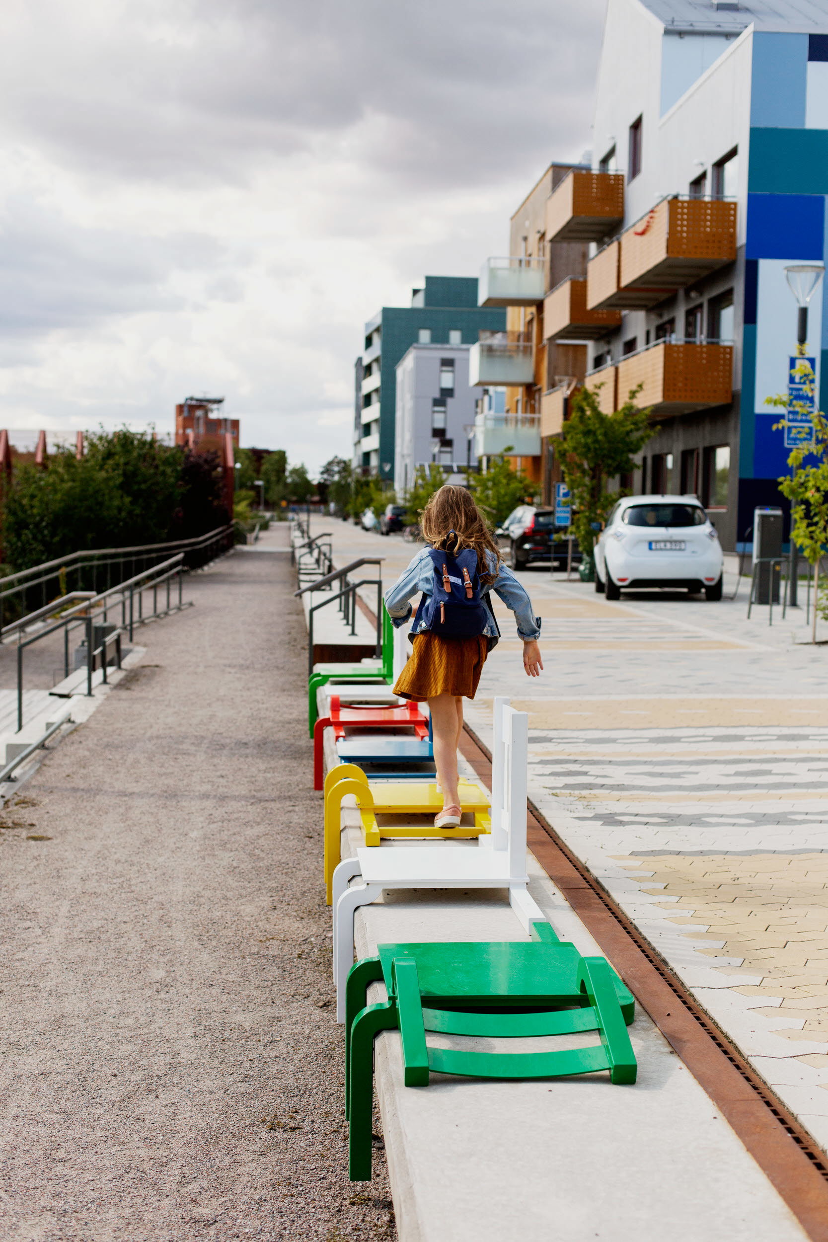 Flicka som hoppar på färgglada stolar längs med ett gångstråk i ett bostadsområde.