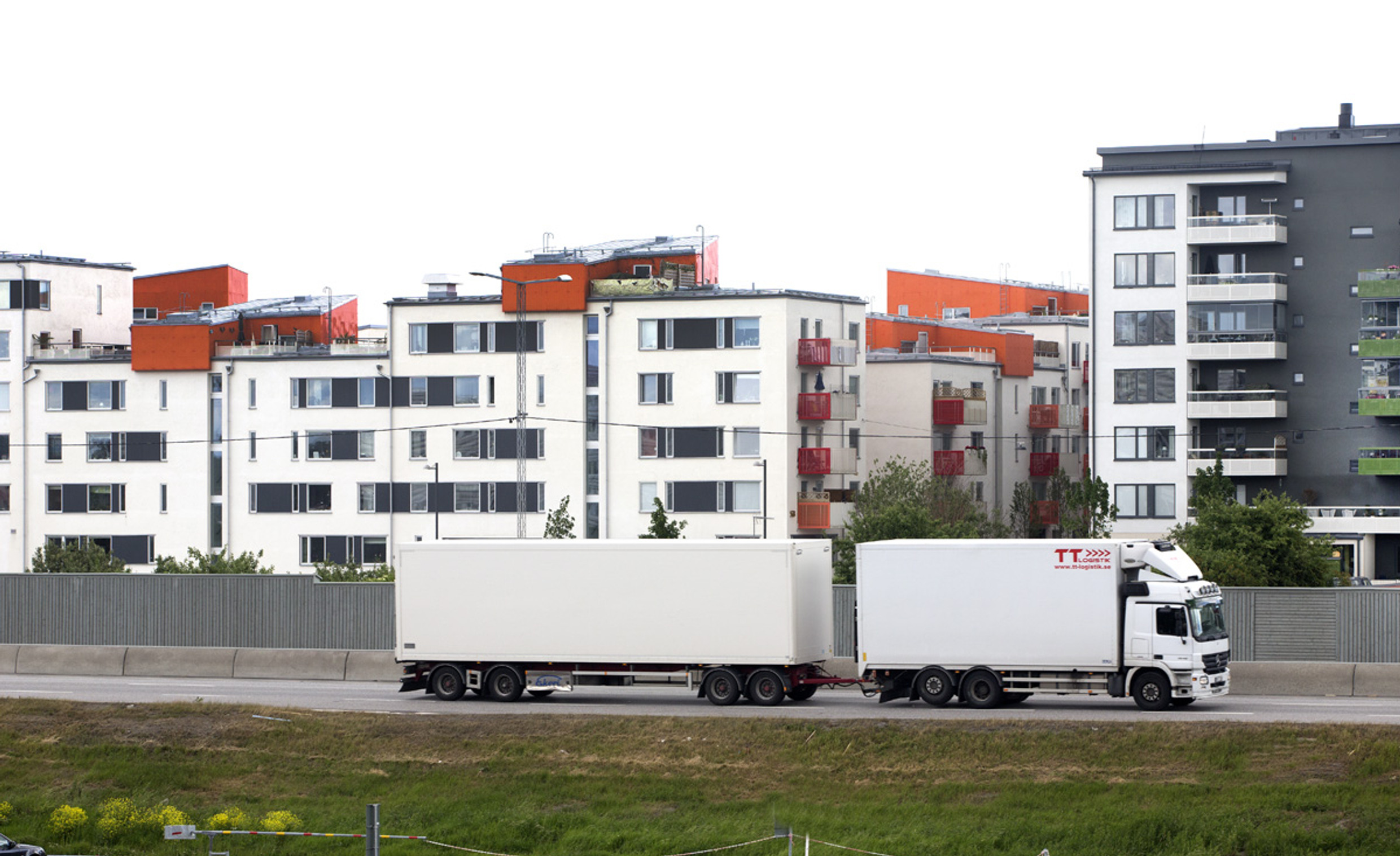 Foto på flerbostadshus med långtradare på en gata intill.