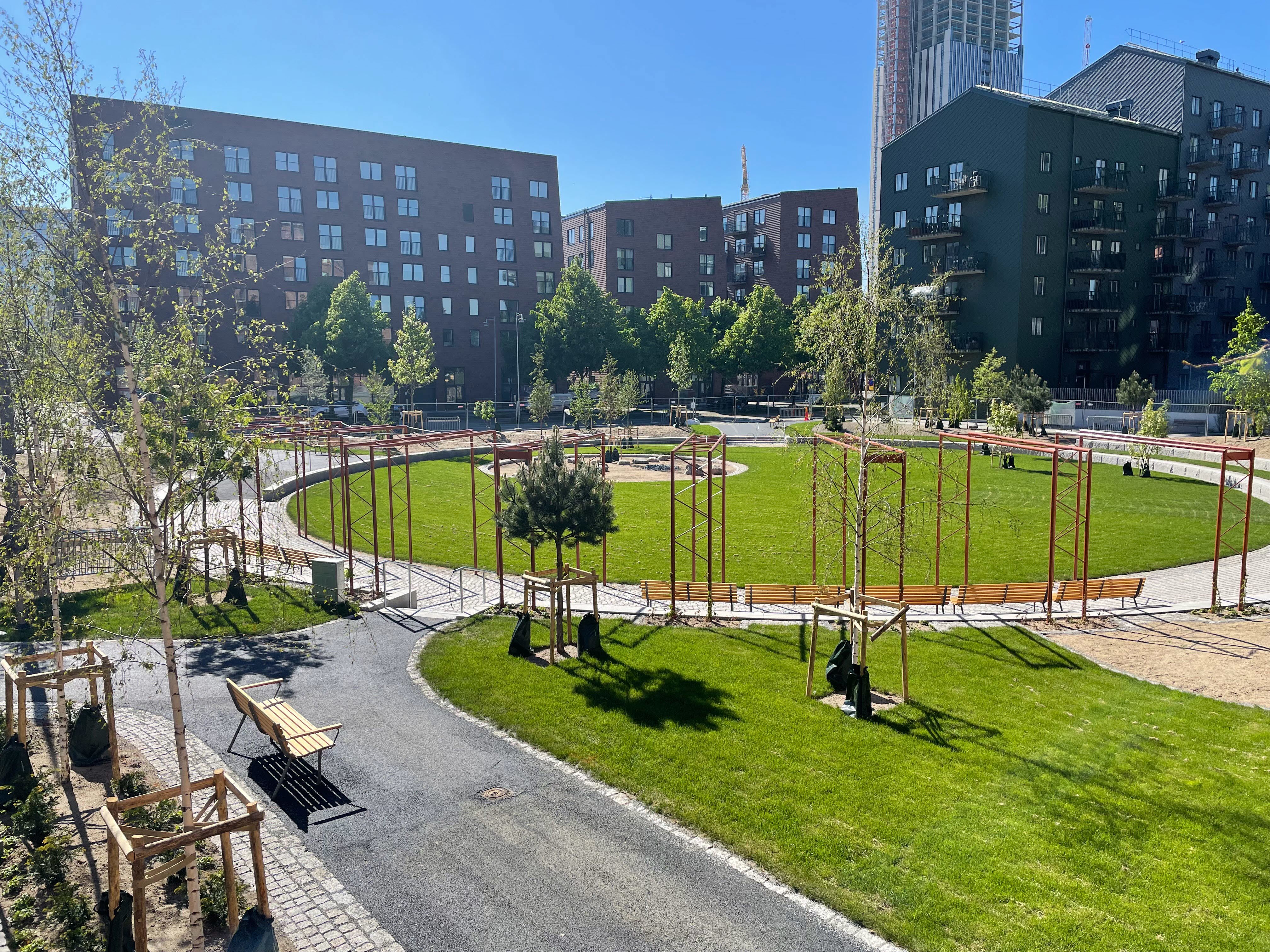 Park med en rund gräsmatta omgivet av högre flerfamiljshus.