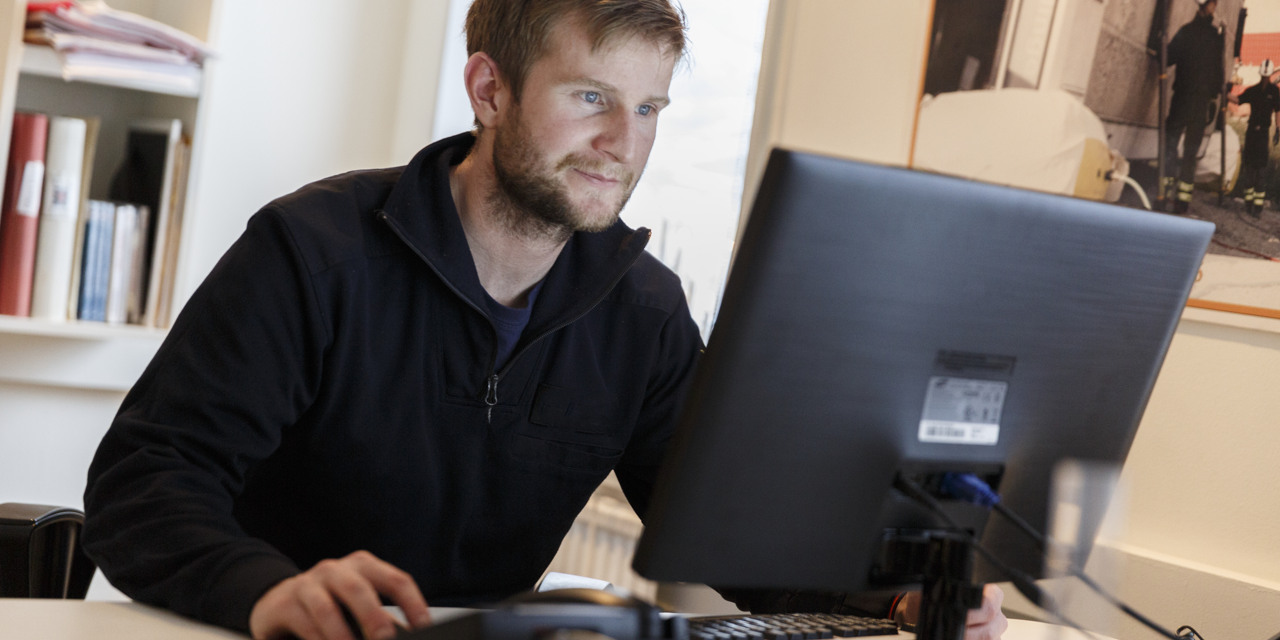 En kille sitter vid ett skrivbord och jobbar med dator.