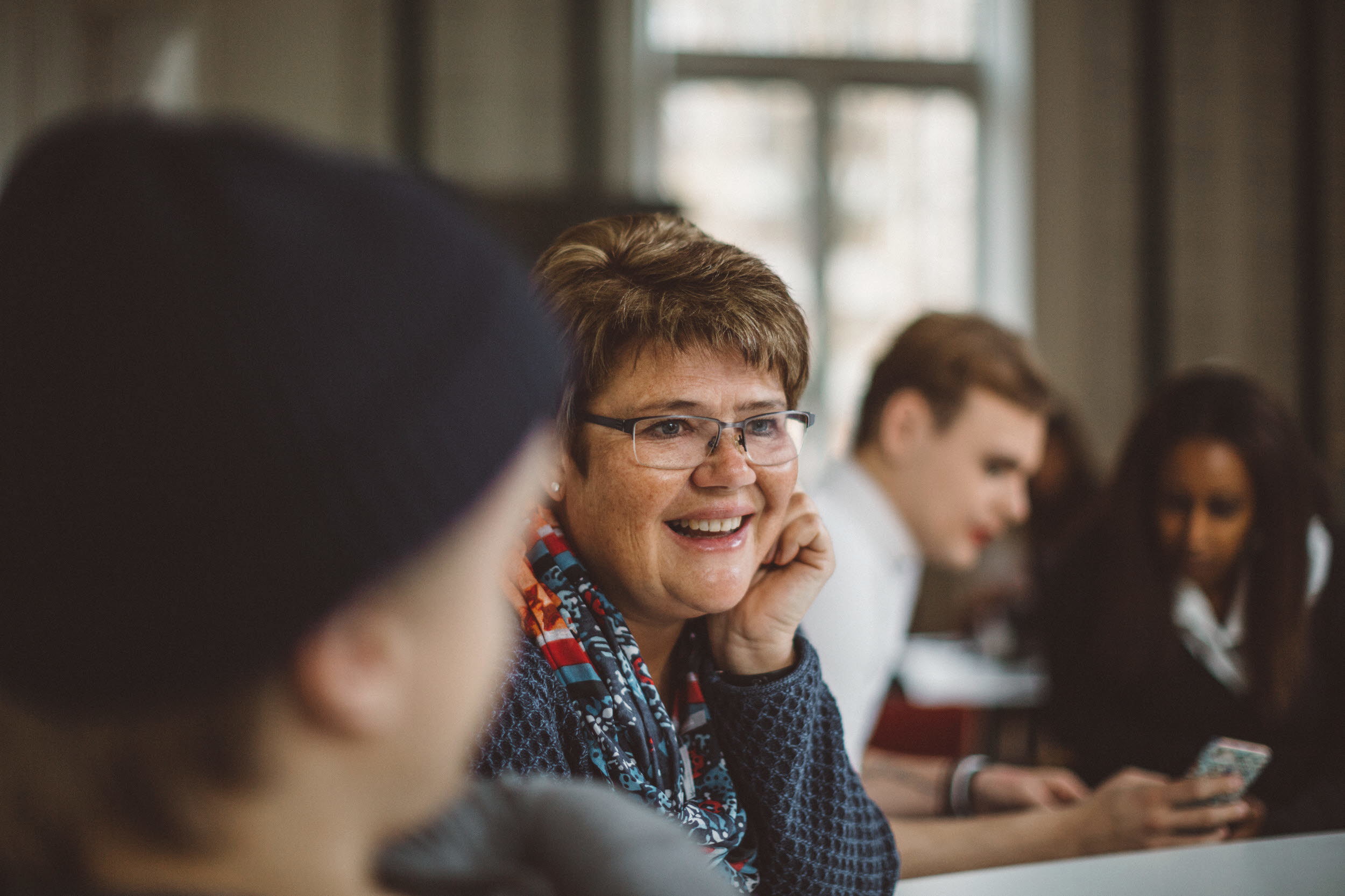 Leende kvinna i diskussion med andra människor.