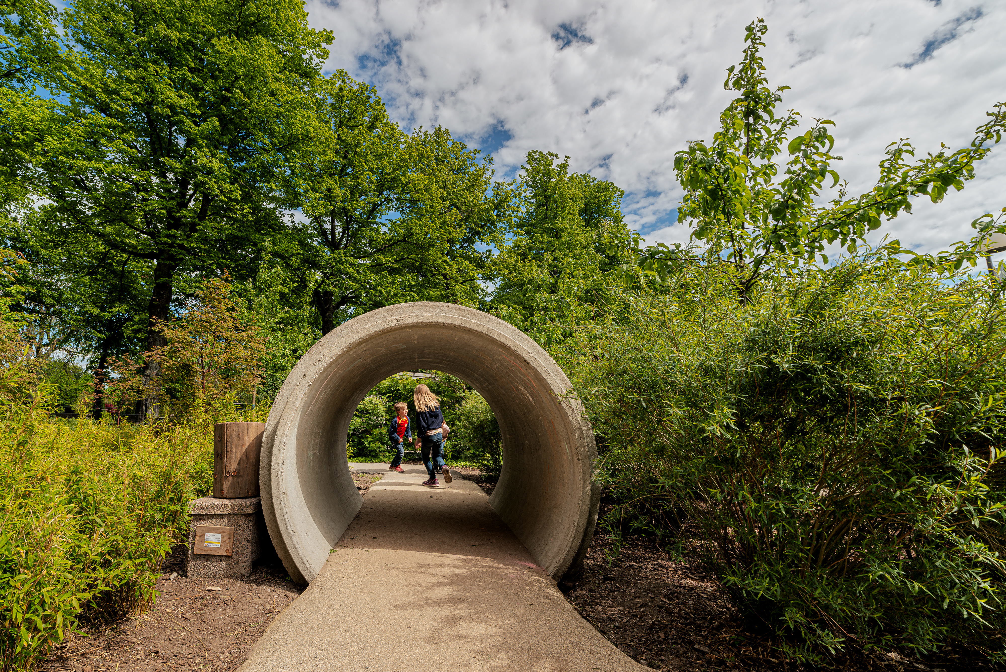 Lekyta utomhus med betongrör man kan springa genom, olika markbeläggningar och växter.