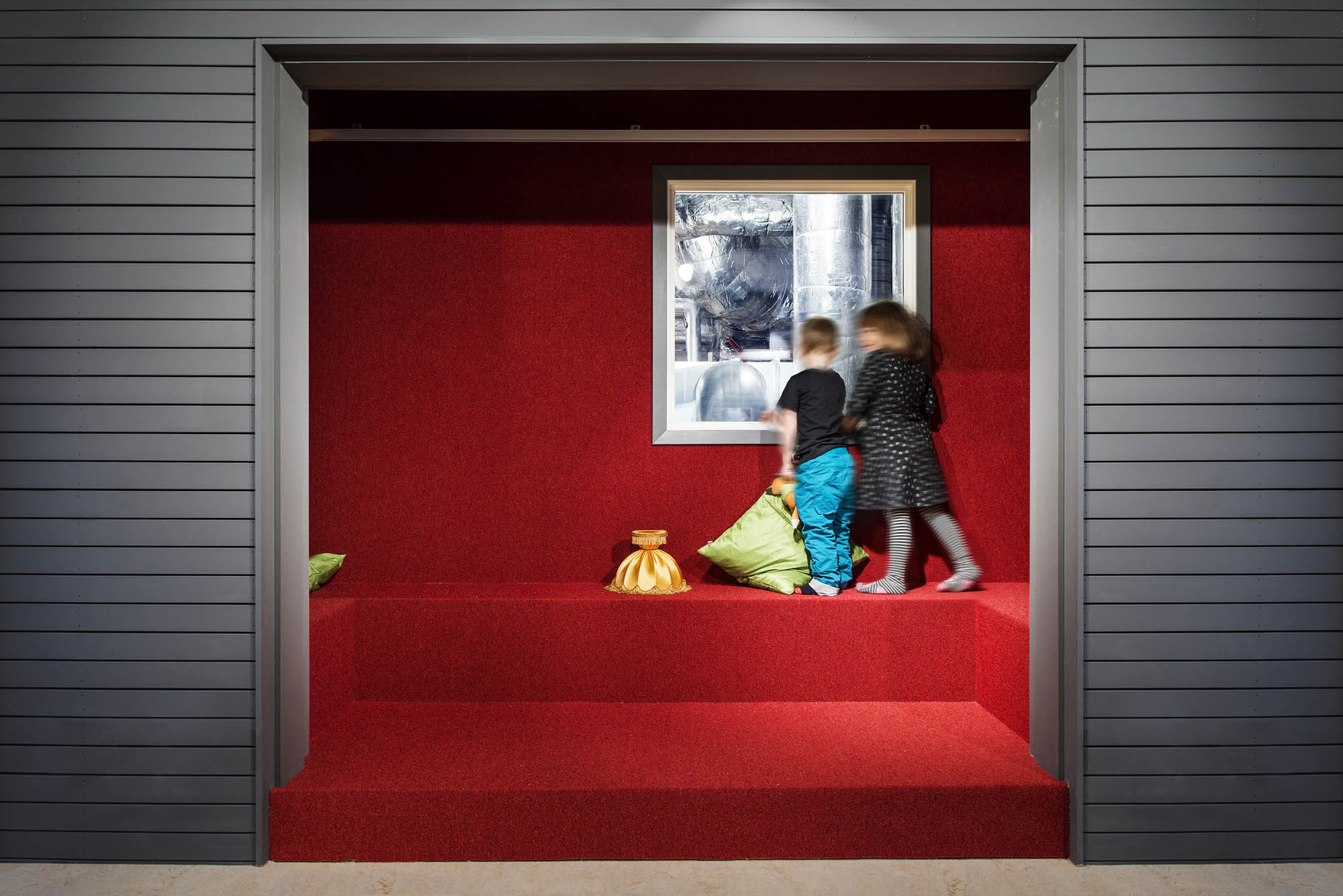 Barn som står i ett rum där golv, väggar och sittplatser är klädda i rött. Panelerna runt omkring är mörkgrå.