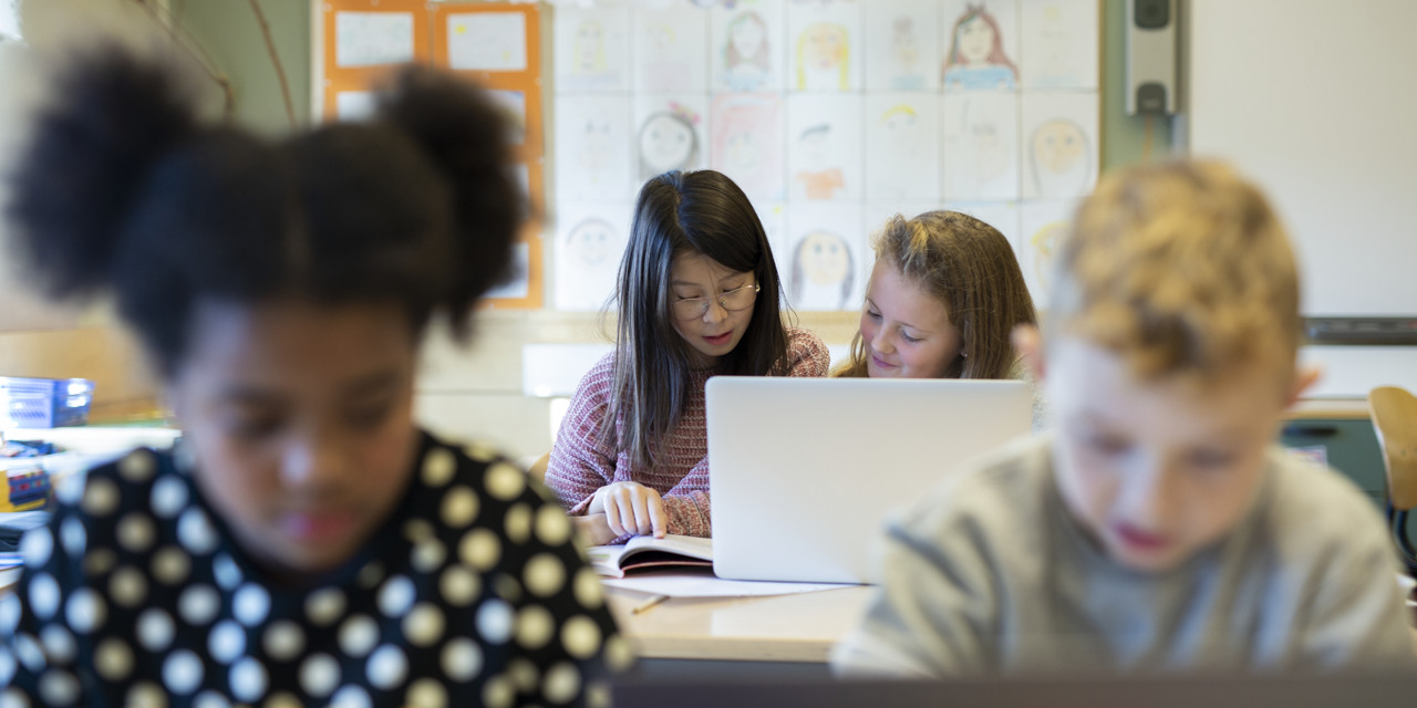 Barn sitter vid bänkar med bärbara datorer.