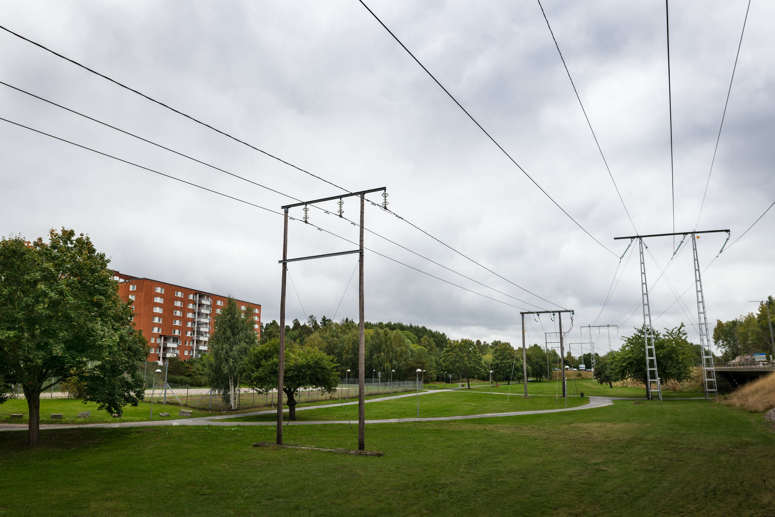 Två olika kraftledningar över klippt gräsmatta i närheten av flerbostadshus.