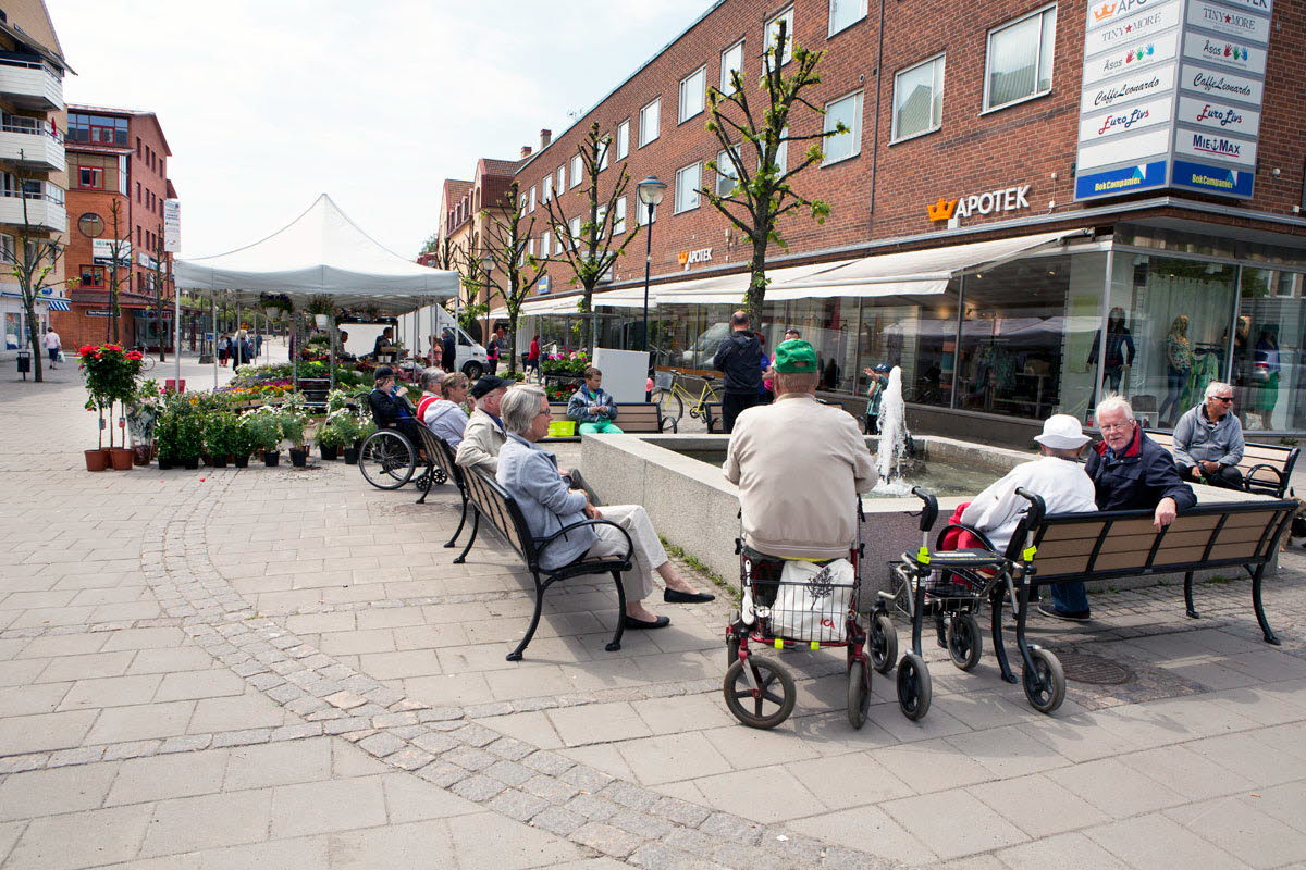 Foto av ett torg med många personer som sitter på bänkar.