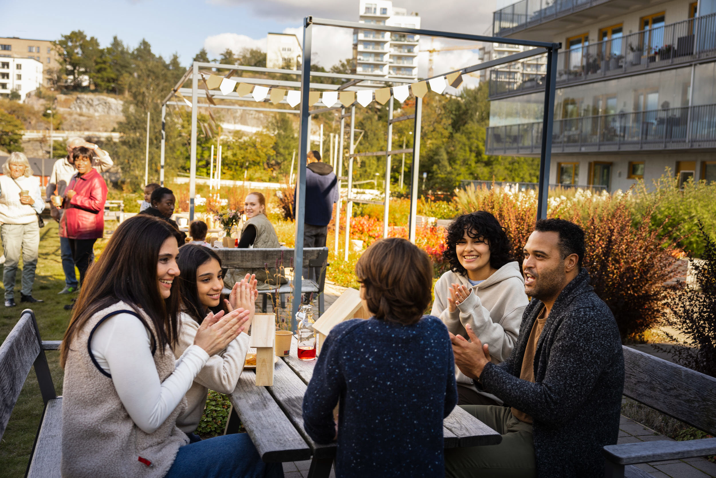 Foto med flera personer som sitter vid ett bord utomhus i ett bostadsområde och samtalar.