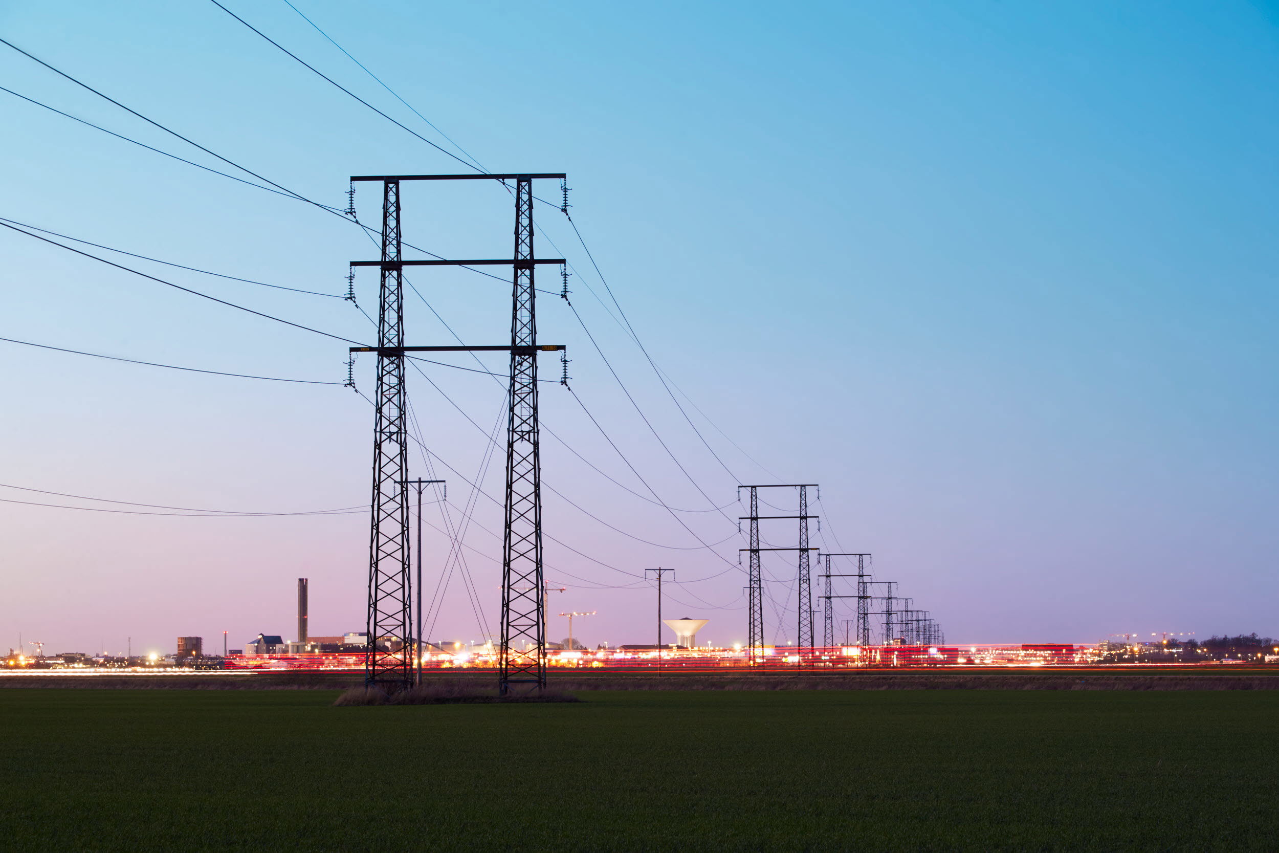 Kraftledningar som passerar bebyggelse. Platt landskap i skymningsljus.