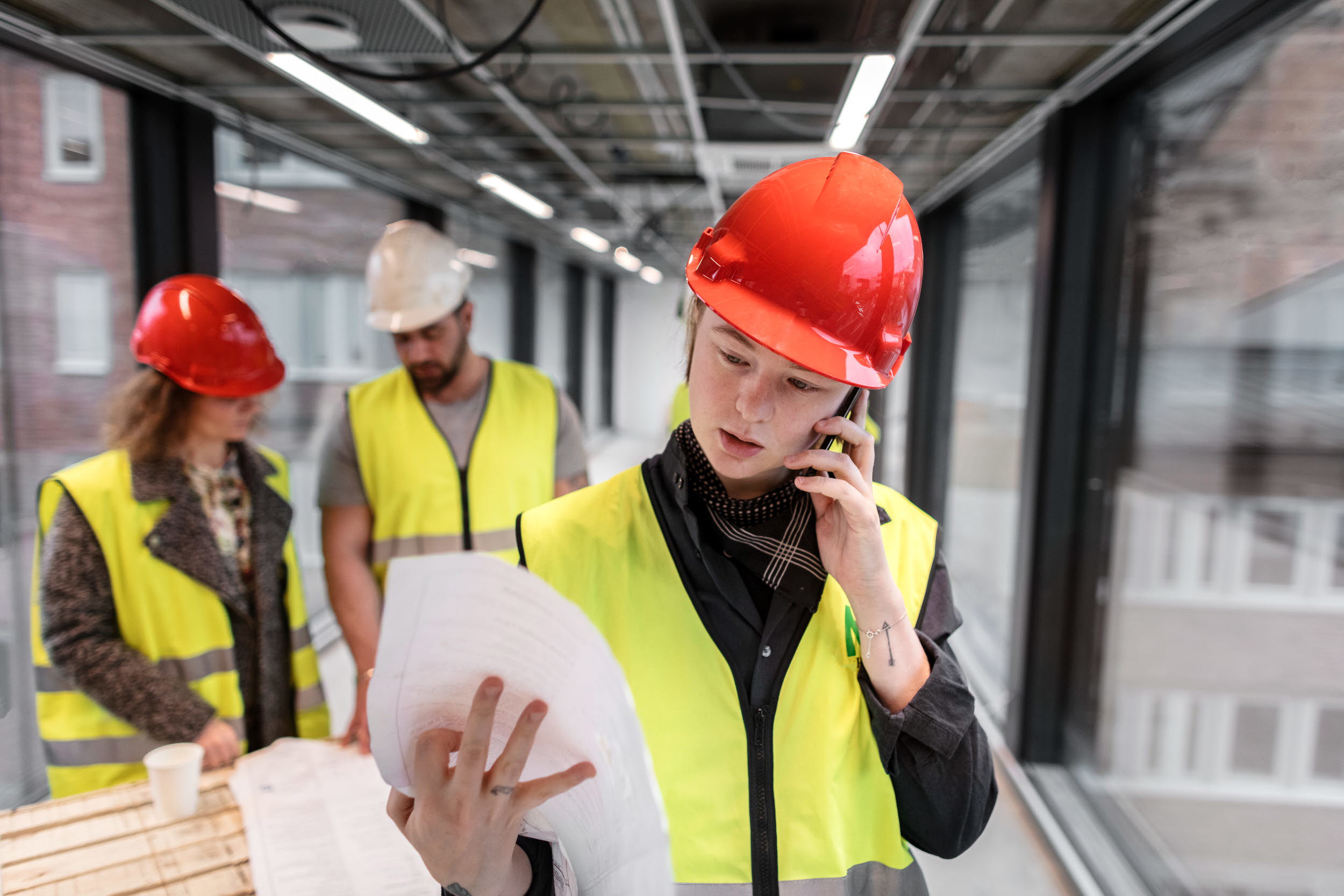 Tre personer läser ritningar på en byggarbetsplats.