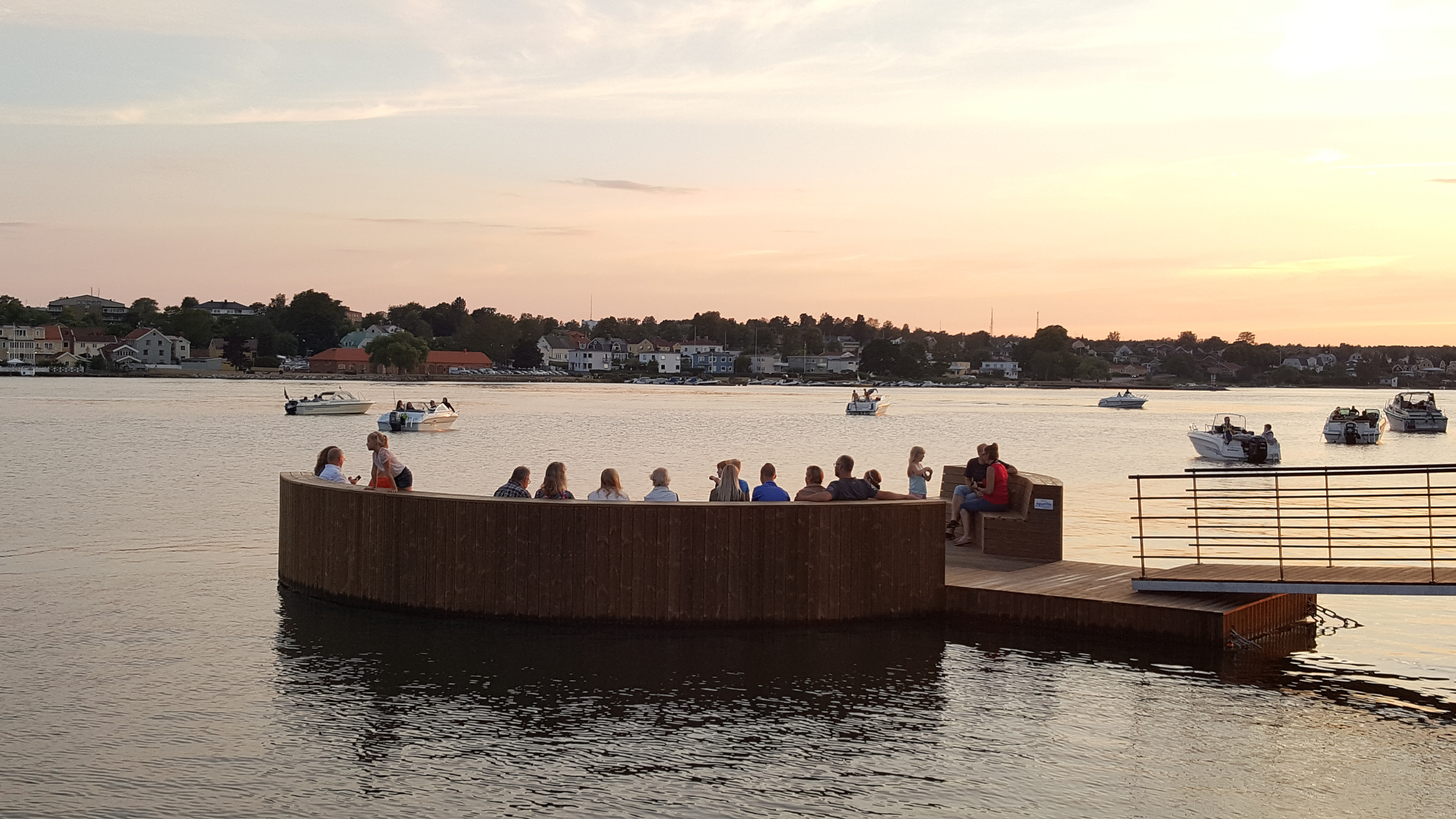 Badbrygga i solnedgång med båtar och stadsvy 