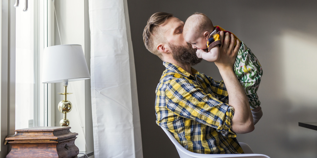 Pappa sitter i en stol och pussar en bebis på kinden.