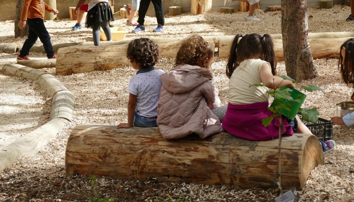Barn som sitter på en stock på en förskolegård.