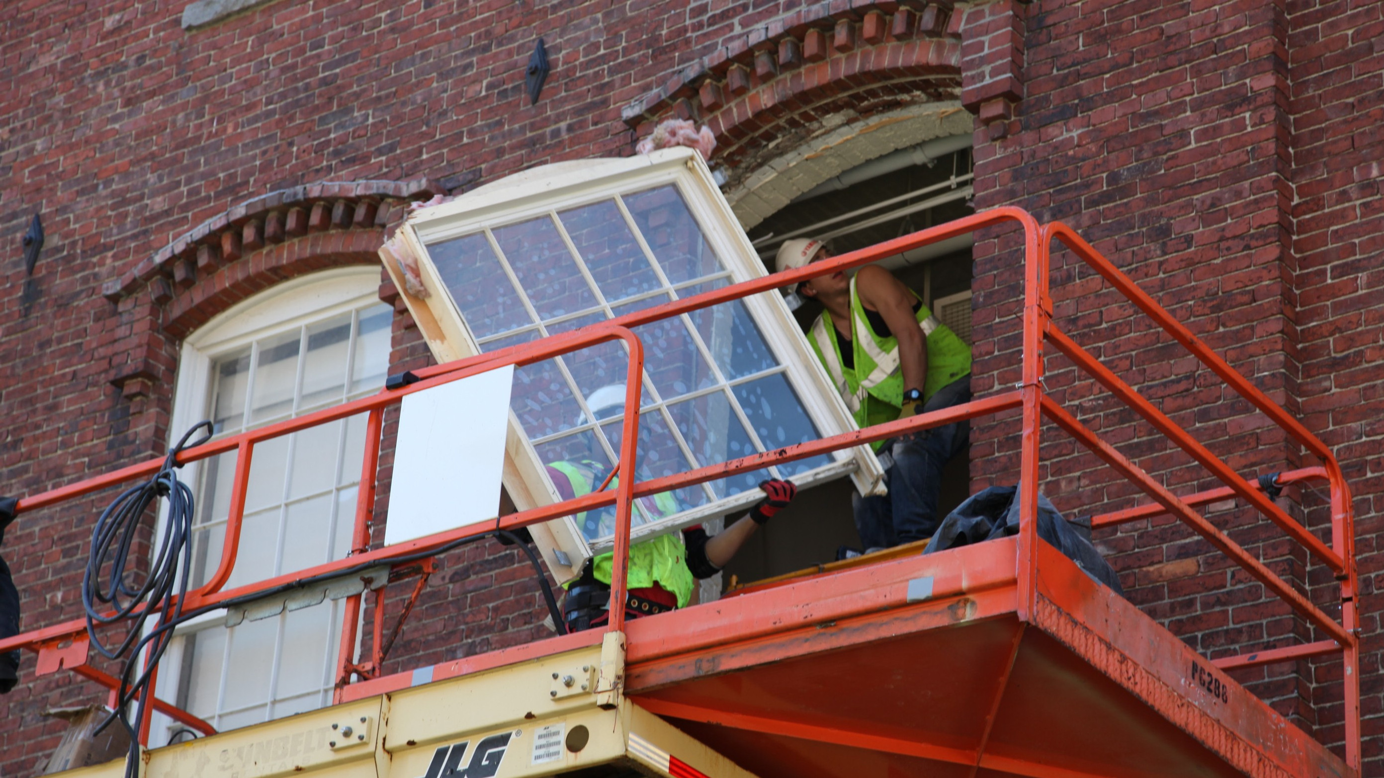 Två personer som byter stort äldre fönster i tegelbyggnad