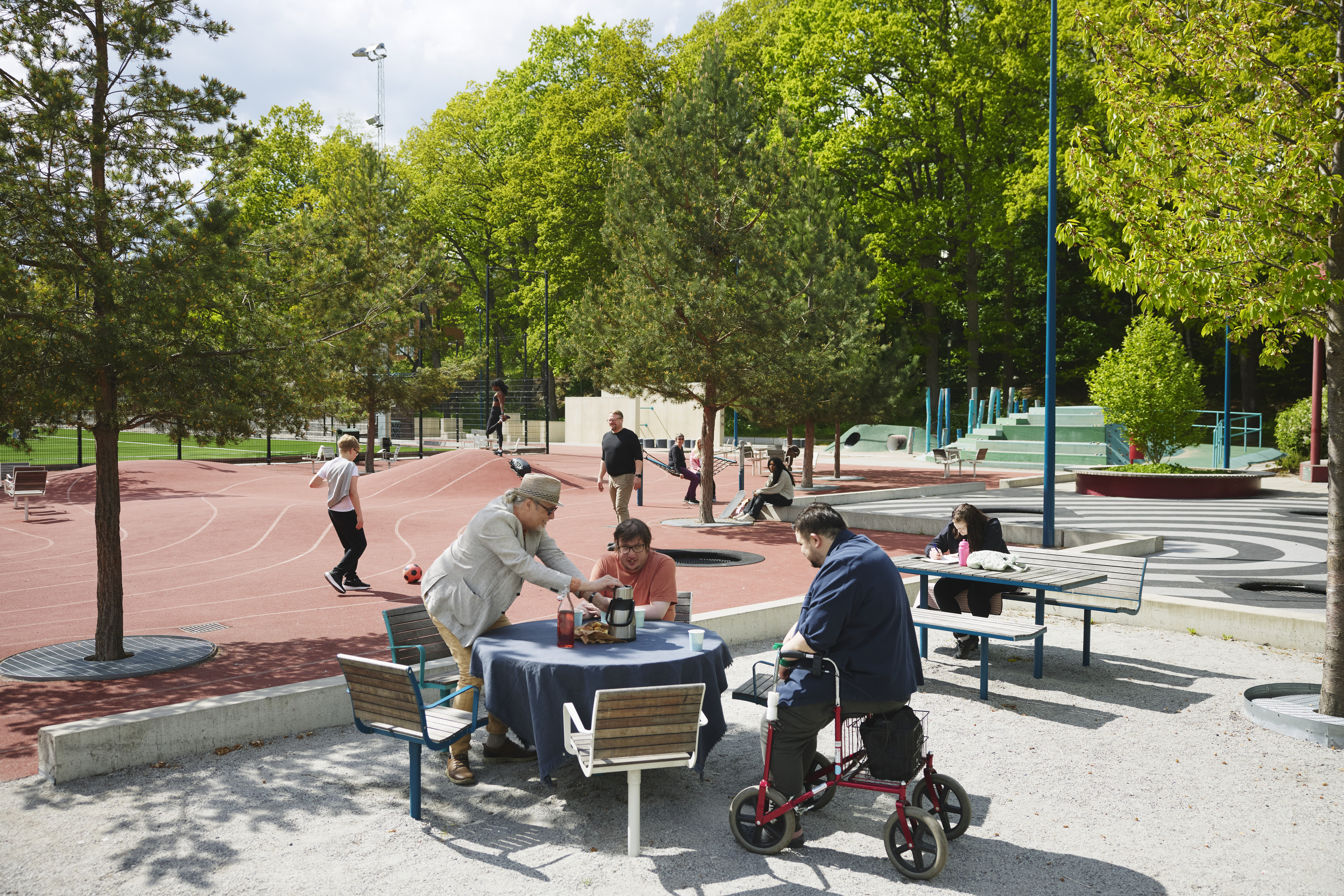 Foto på personer som sitter vid bord och samtalar i en grön parkmiljö.