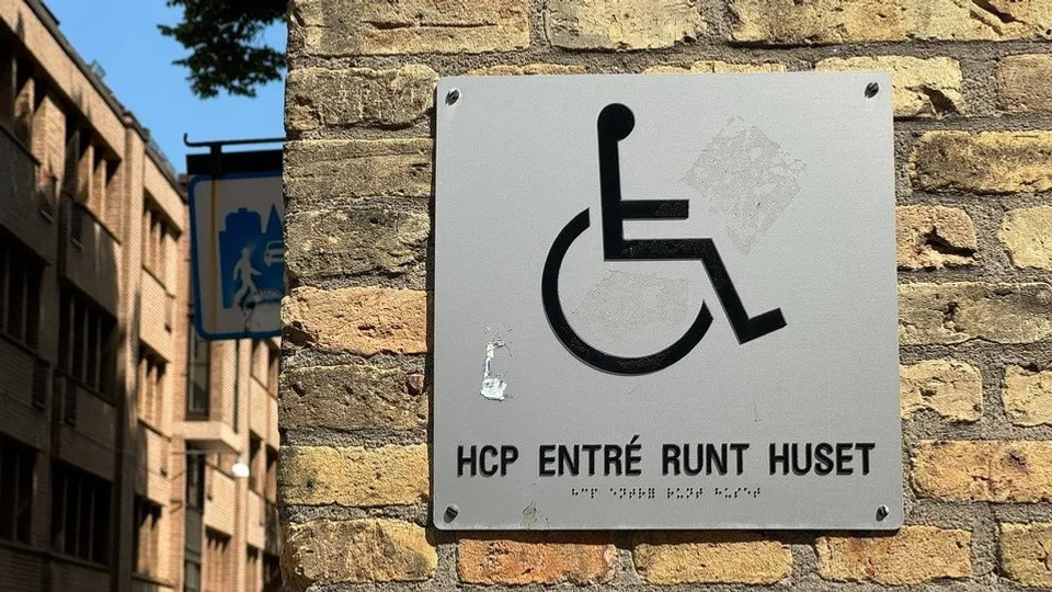 Foto på skylt på tegelvägg med rullstol och texten "HCP-entre runt hörnet". 