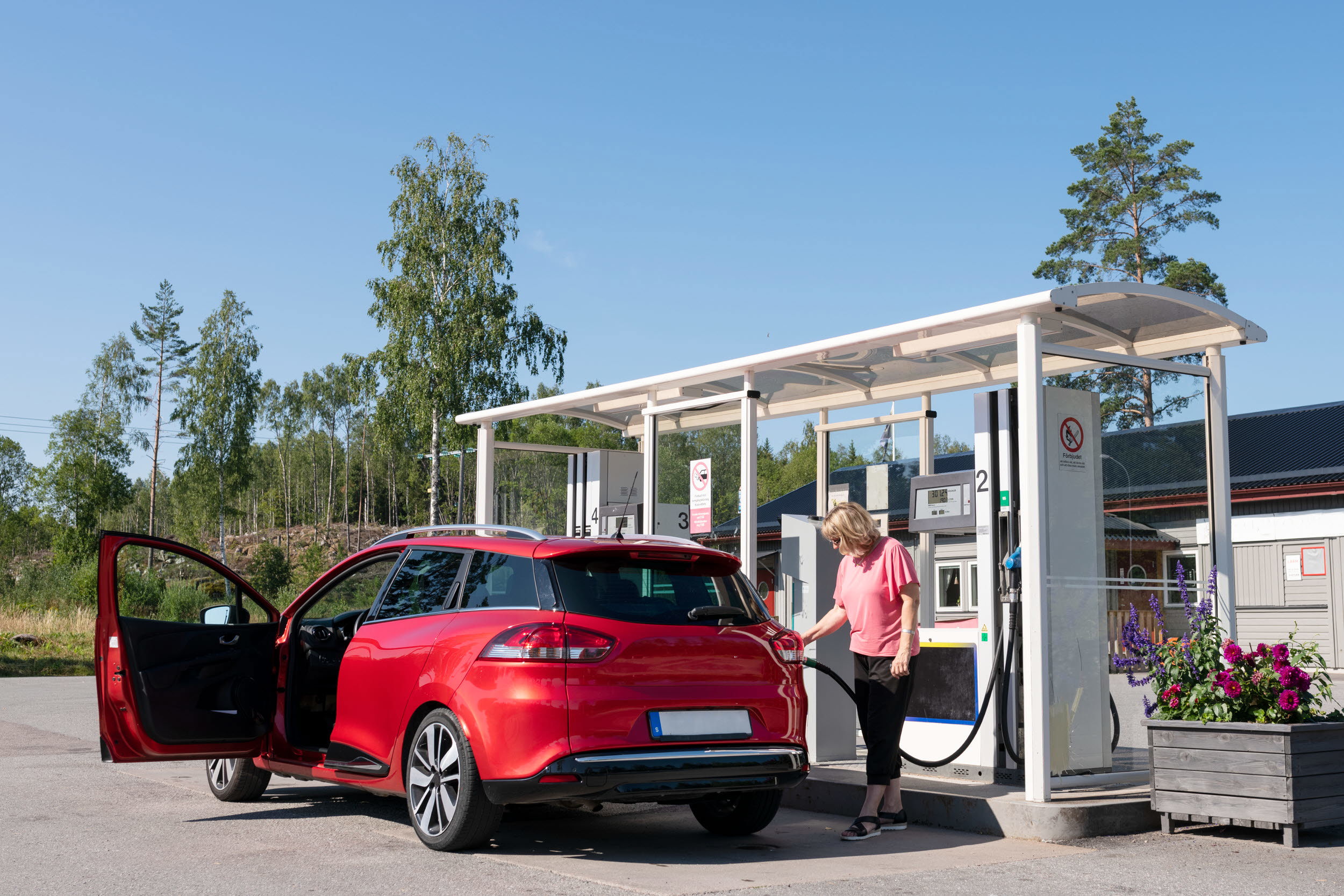 En person står och tankar en röd bil vid en pump.