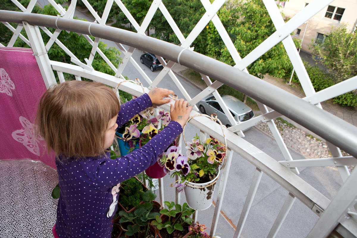 Liten flicka står på balkong och tittar på blommor.
