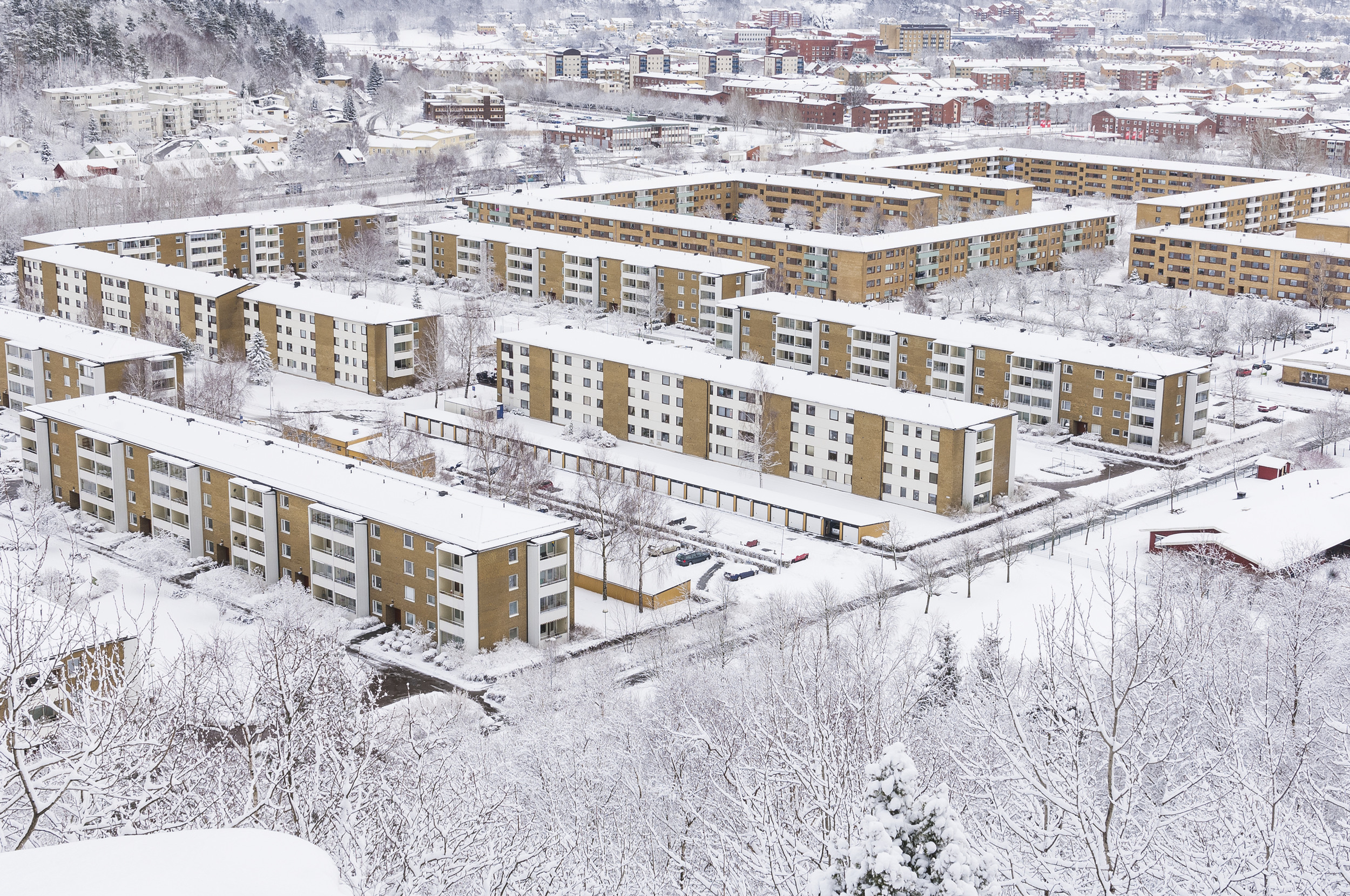 Snötäckt flerbostadsområde med flera hus och grönområde.