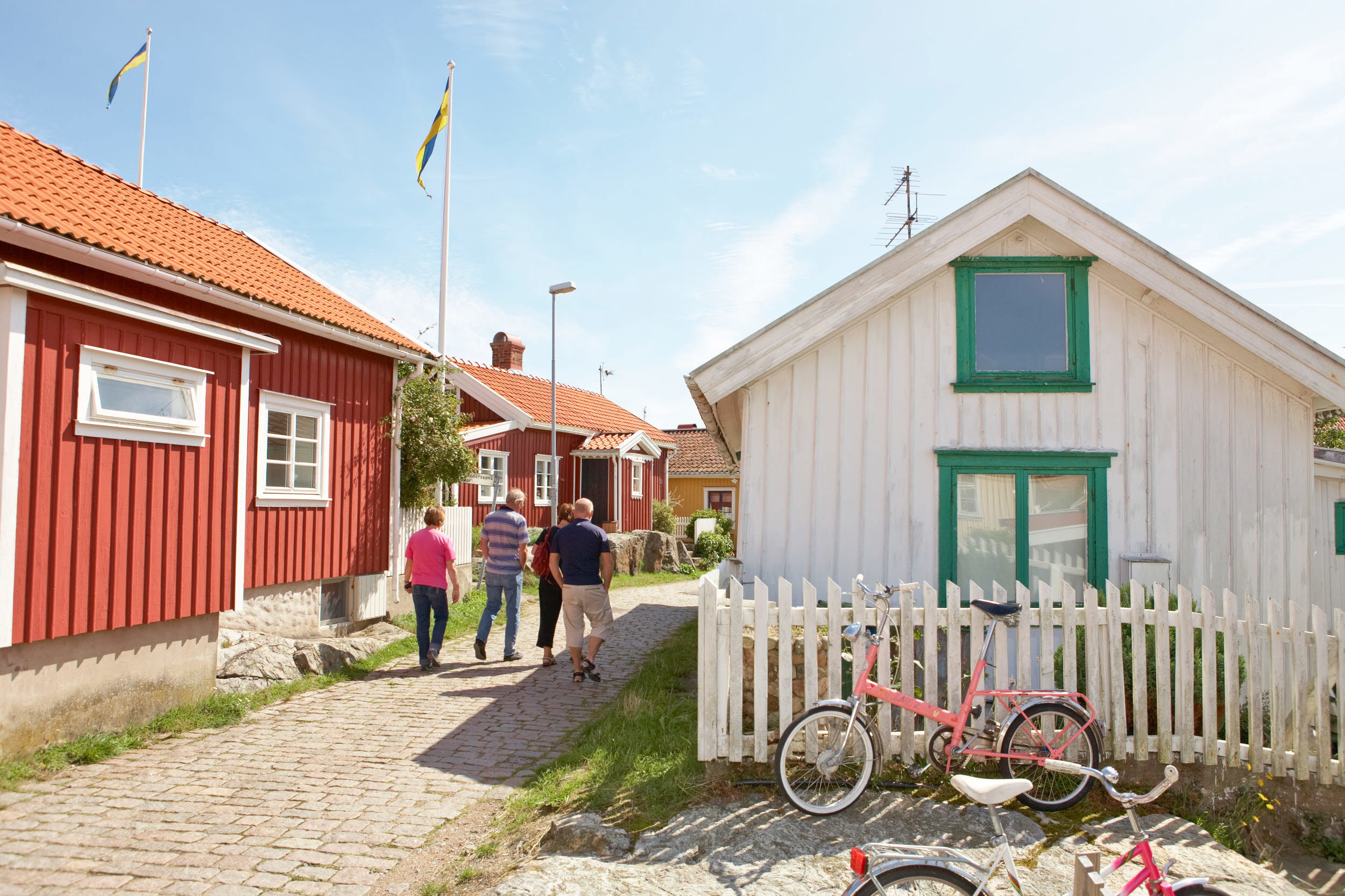 Fyra personer vandrar längs kullerstensgator i en kulturmiljö bland röda och vita trähus. Foto: Anders Järkendal/Scandinav