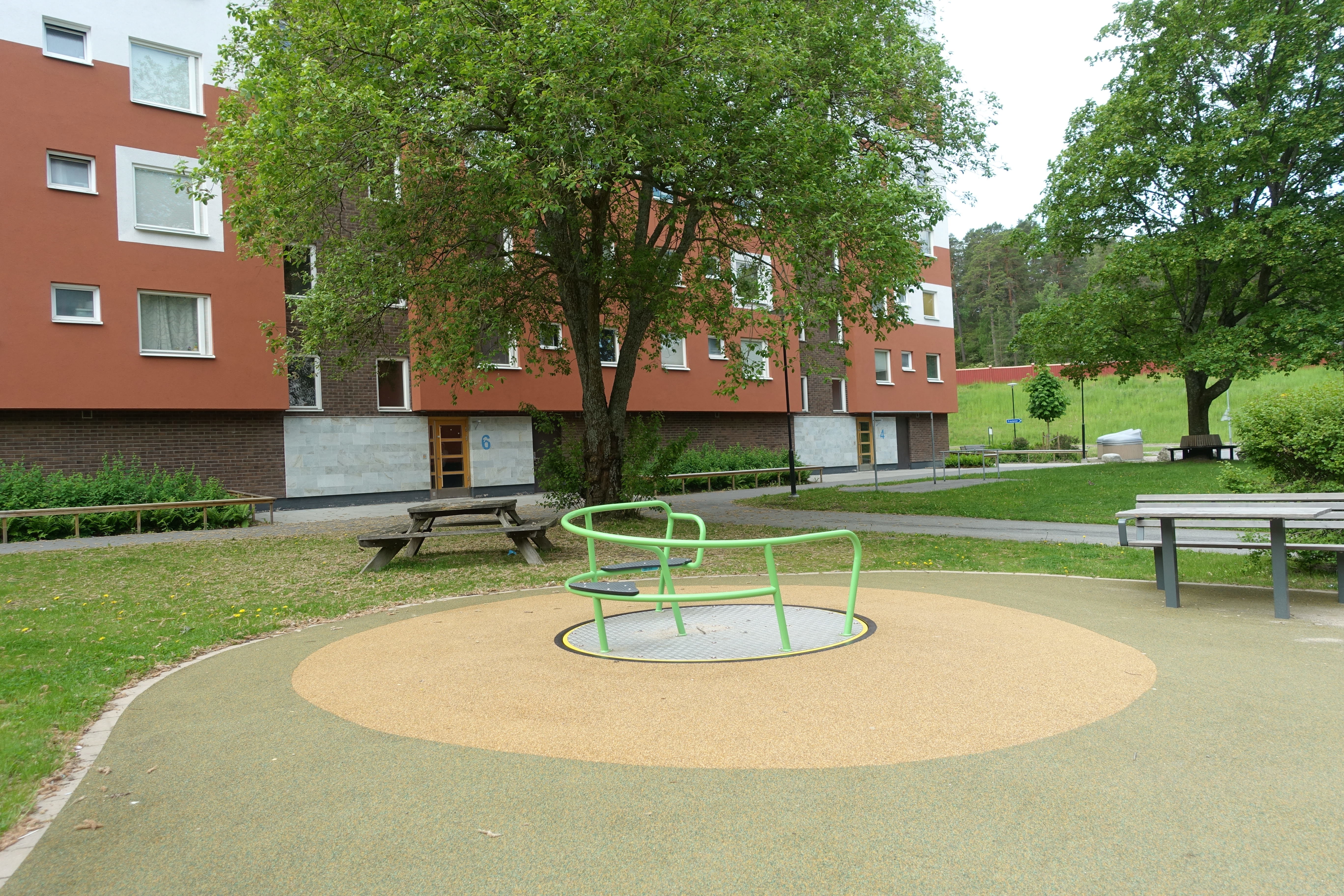 Buskar, träd och utemöbler på en innergård vid ett flerbostadshus. Foto: Ida Jonskog/Boverket.