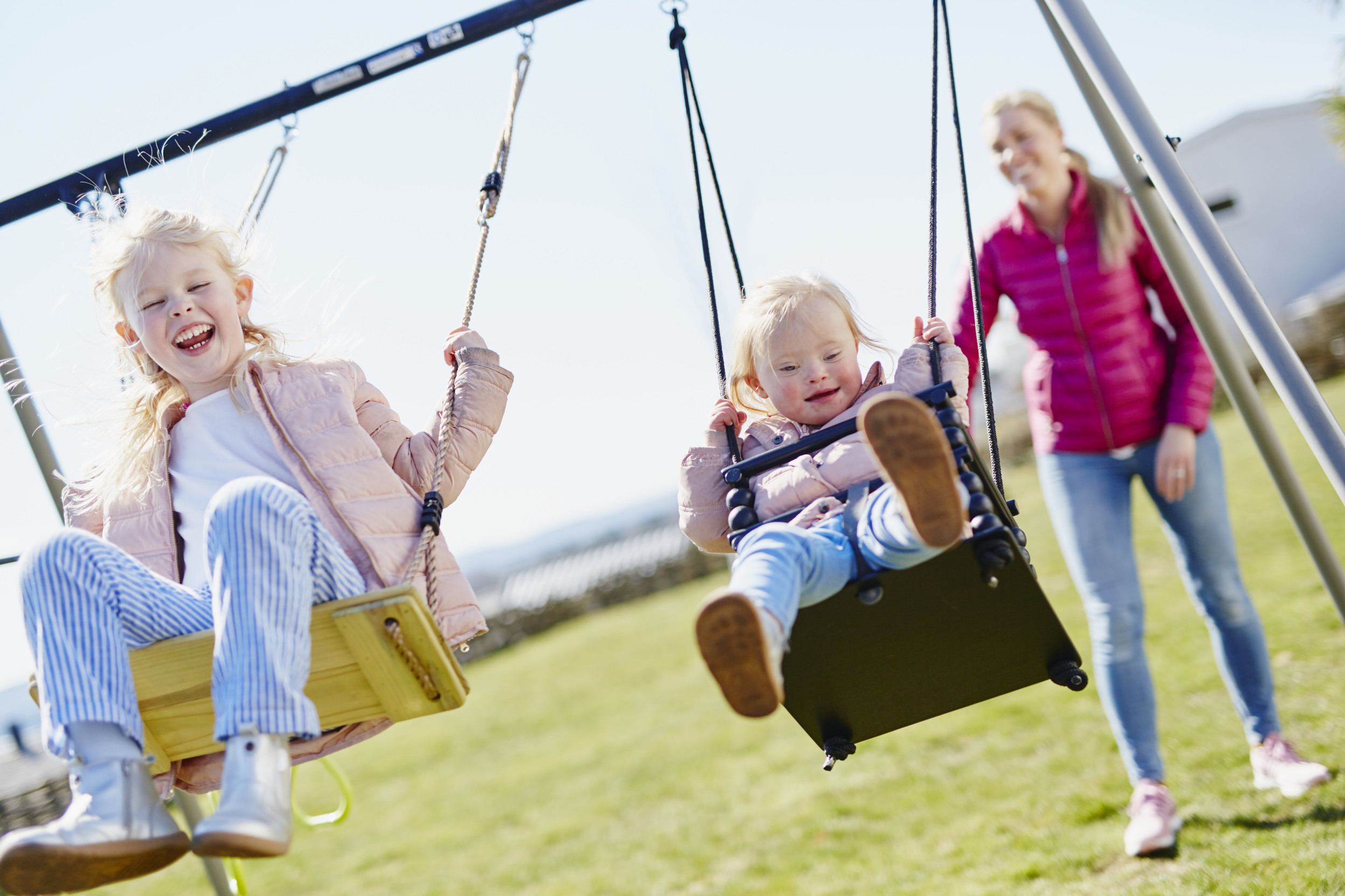Två barn gungar i lekpark med sin mamma.