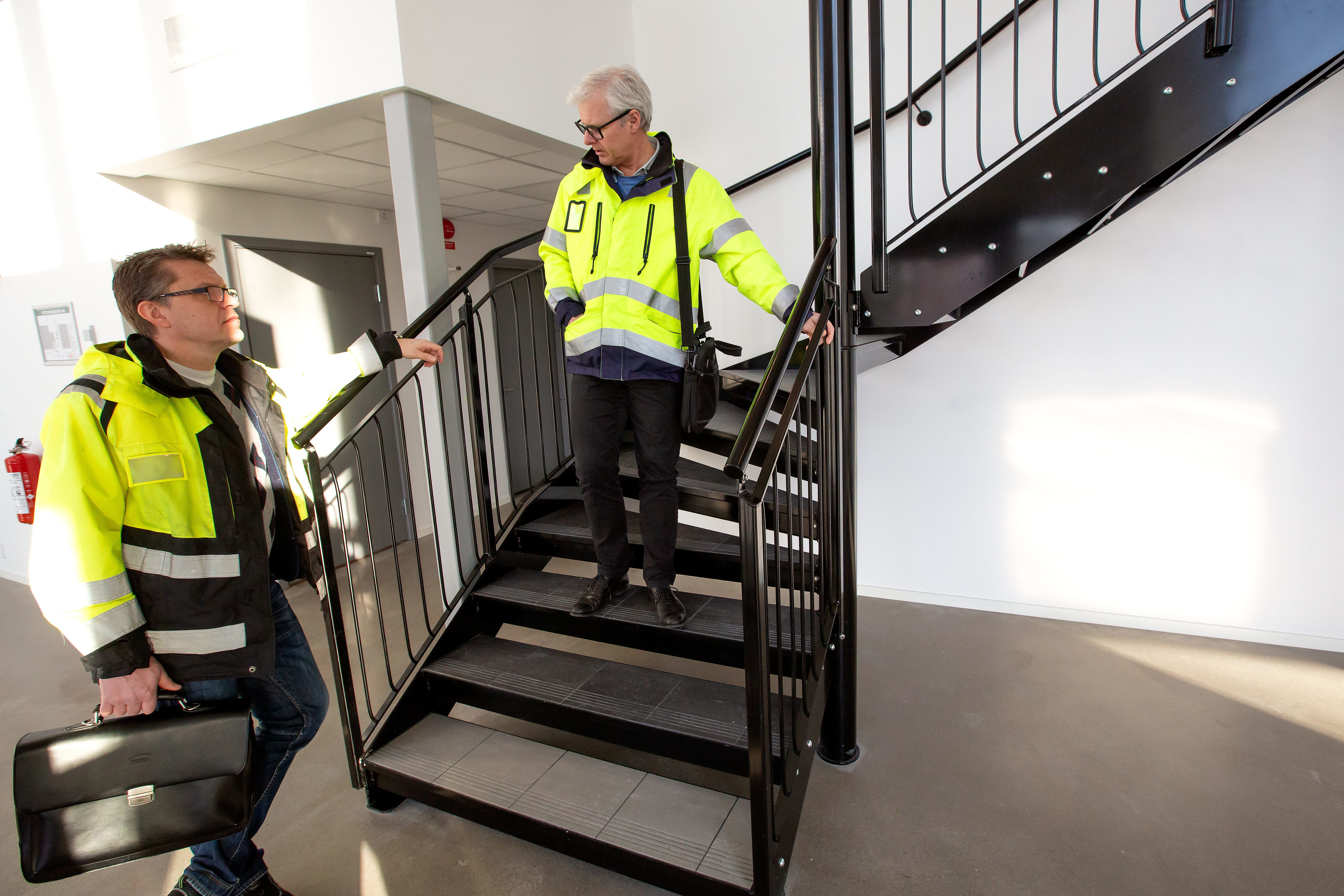 Foto på två män i arbetskläder som står och pratar i en trappa.