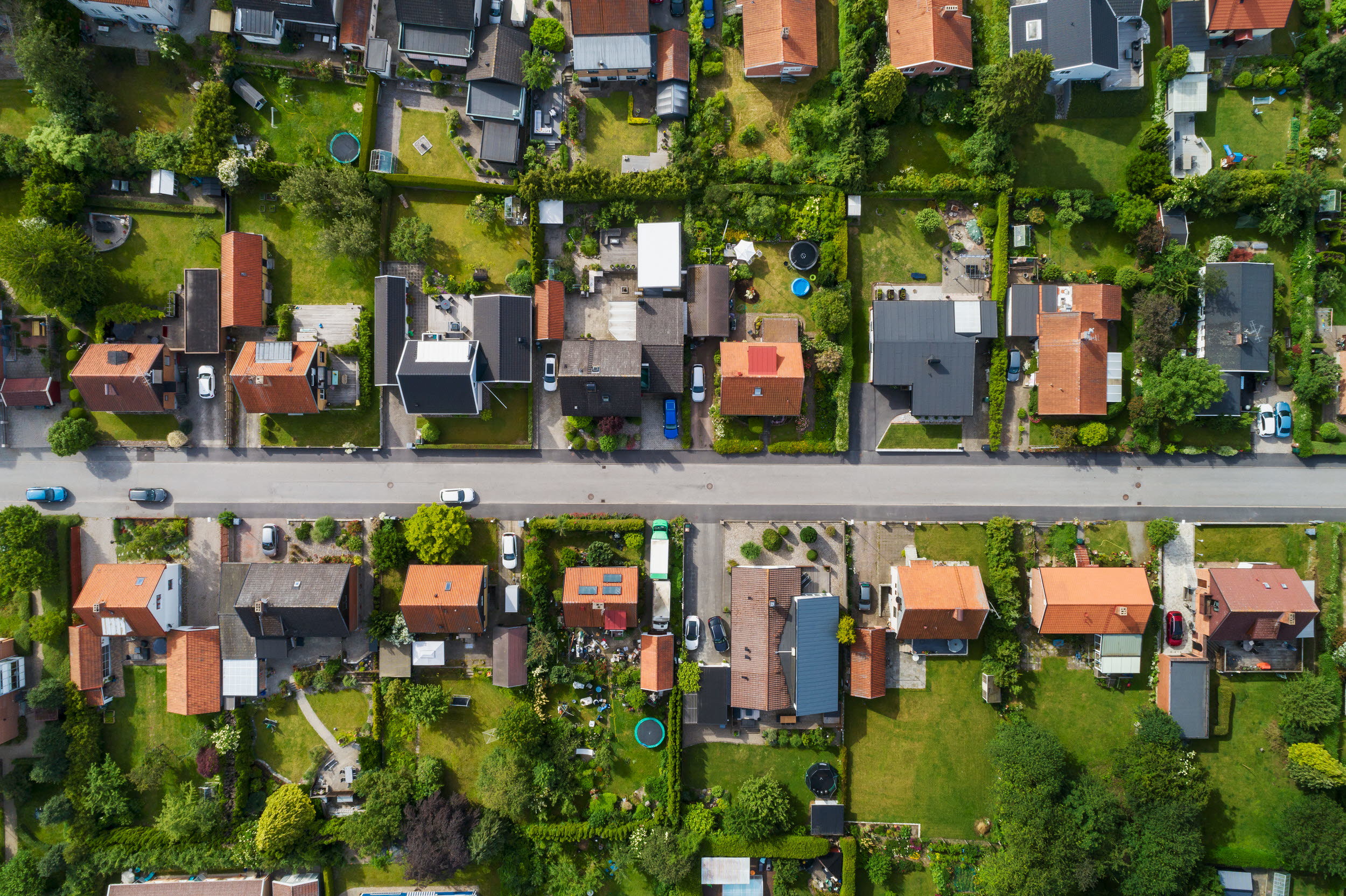 Flygbild på villor med trädgårdar längs en gata
