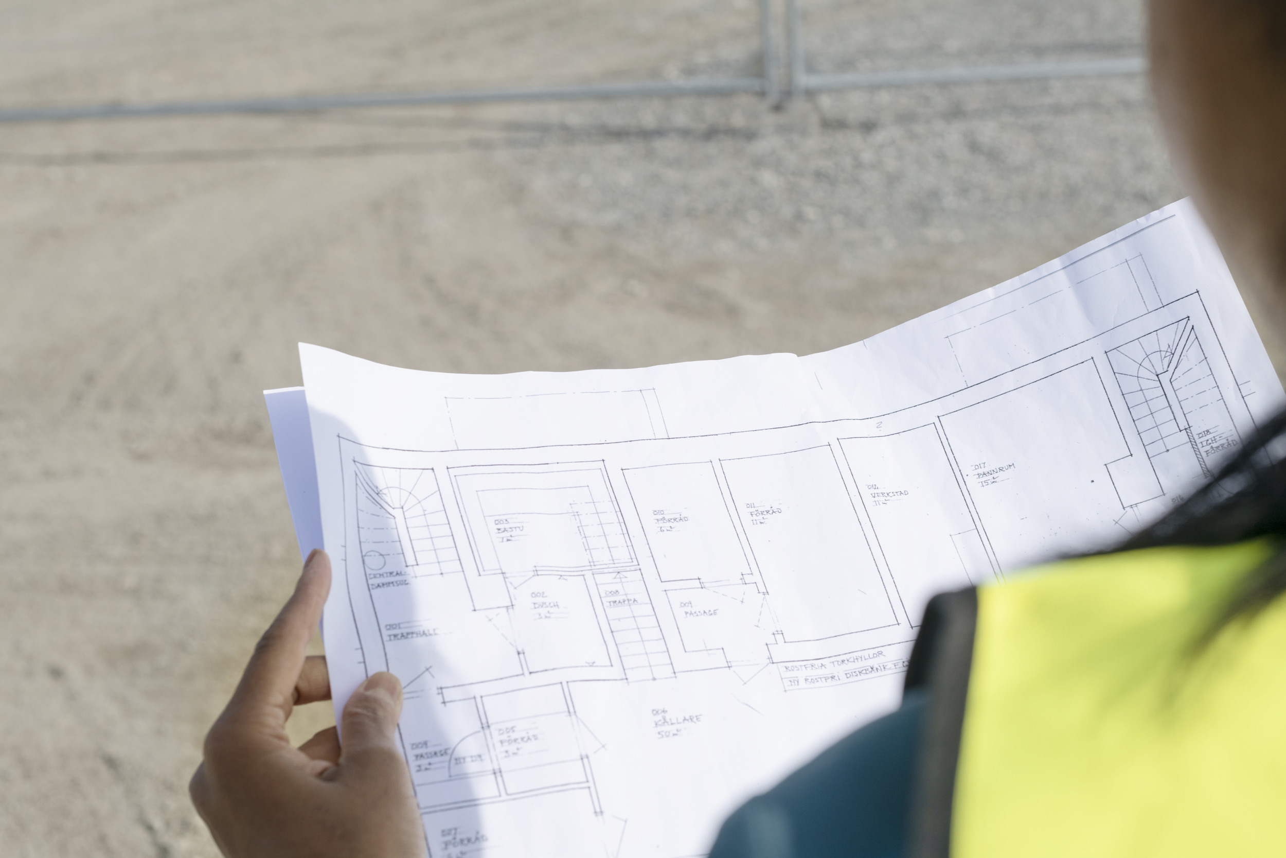 En person i gul skyddsväst tittar på en ritning. 