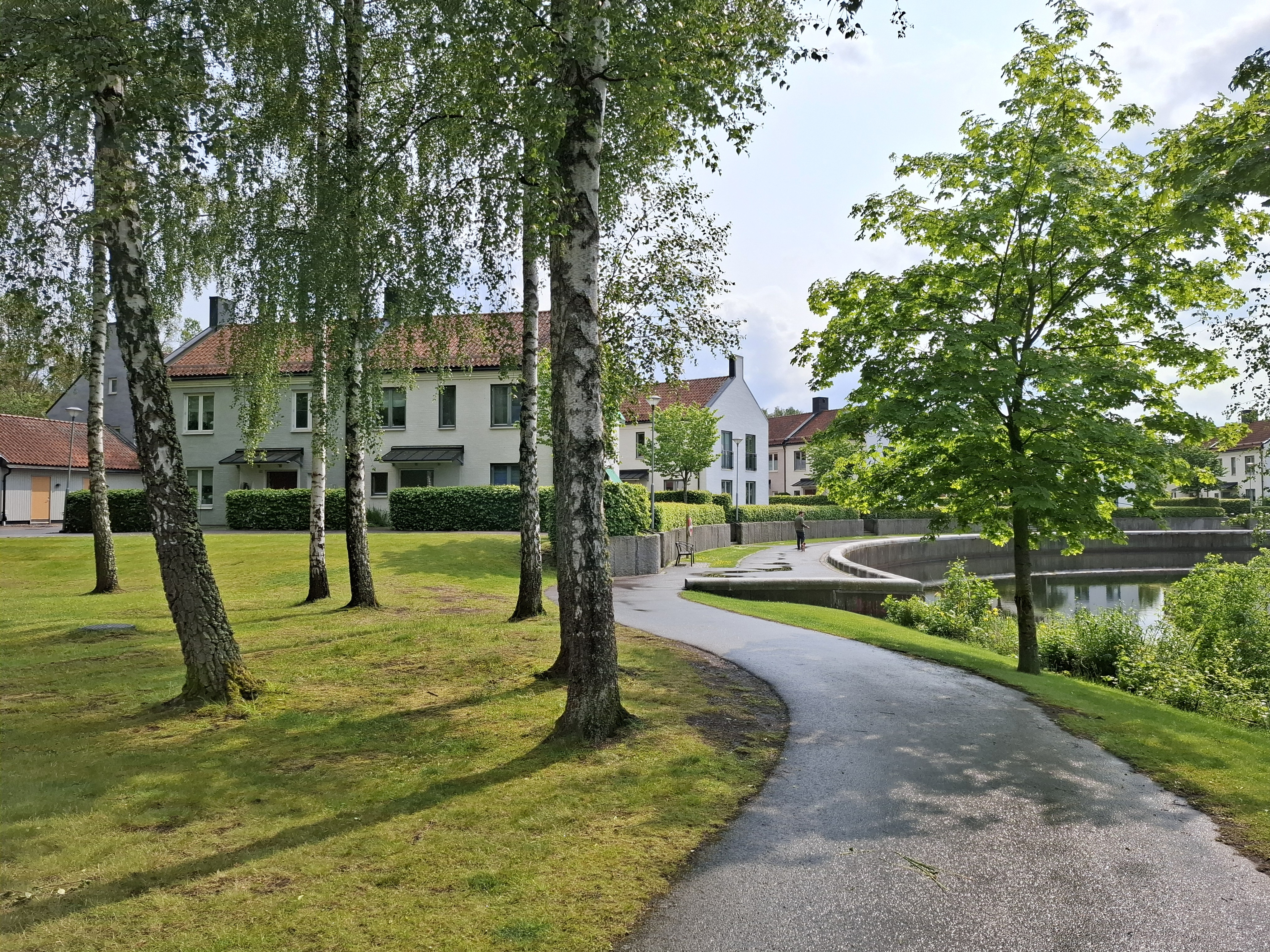 Tvåvåningsbebyggelse av bostäder i anslutning till en grönskande park med en damm.