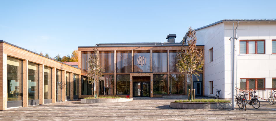 Foto på stenlagd skolgård med skolbyggnad.