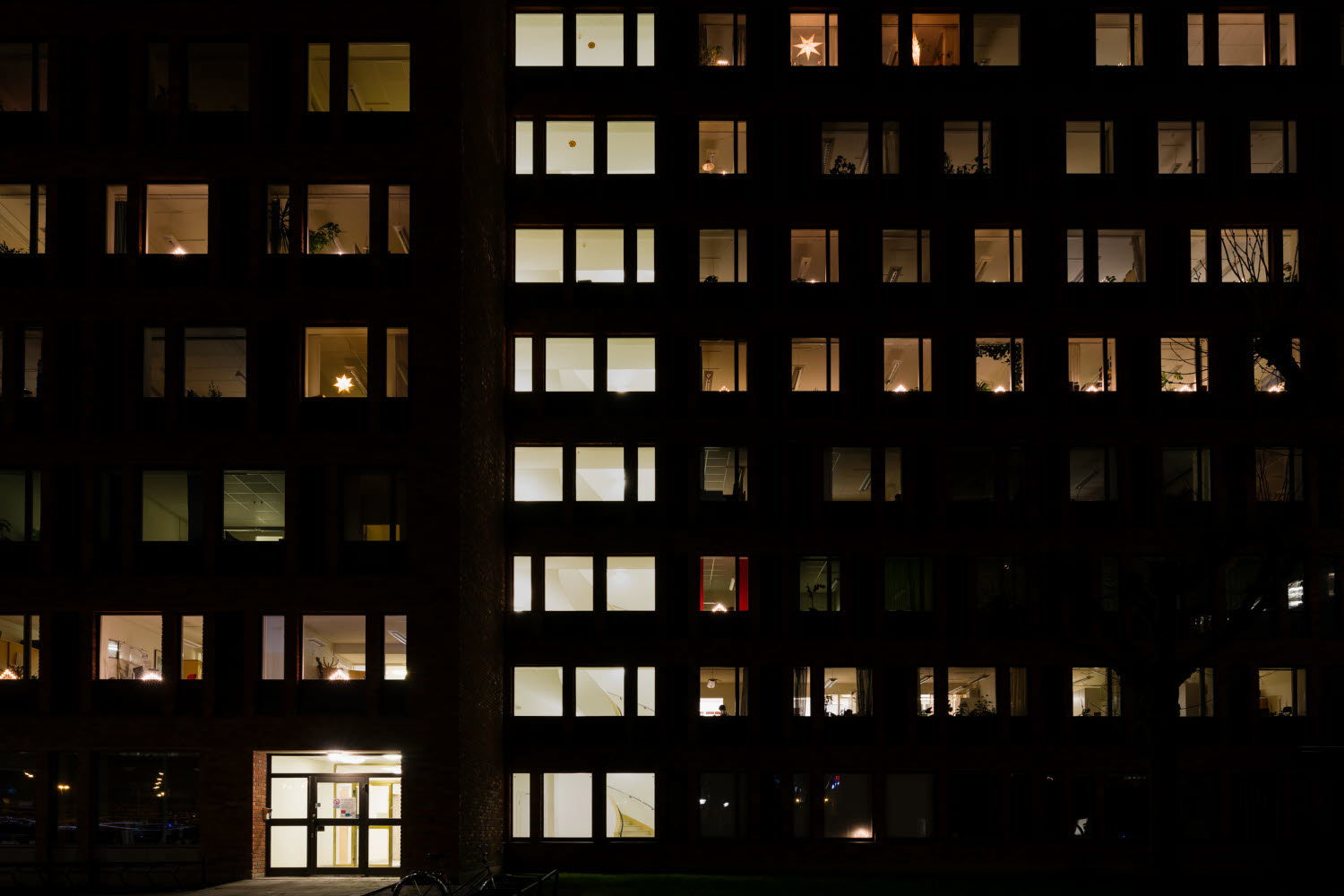 Bild på ett flerbostadshus i mörker med upplysta fönster.