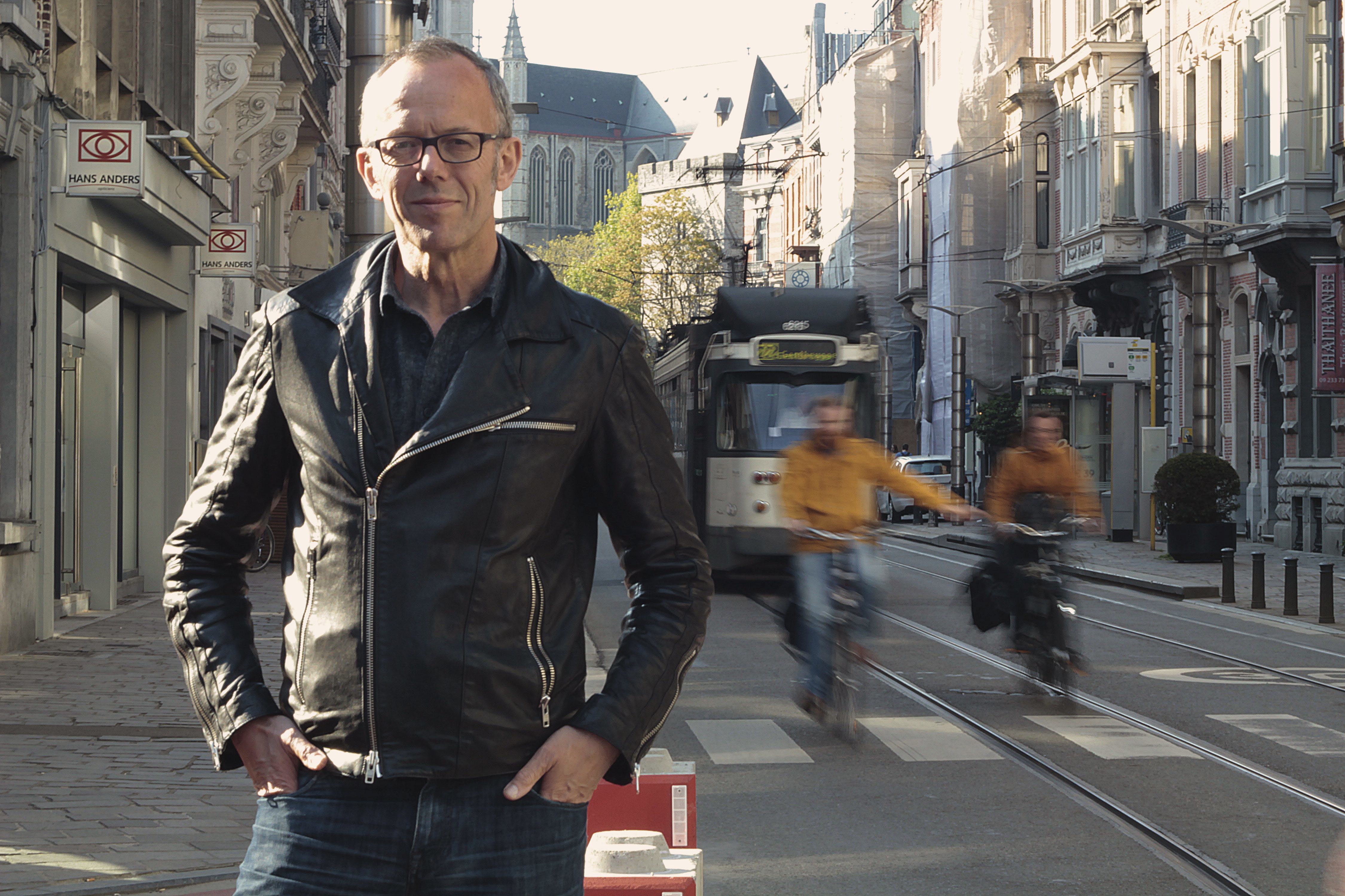 Porträttbild av Filip Watteeuw, biträdande borgmästare i Gent. I bakgrunden finns cyklister och buss. 