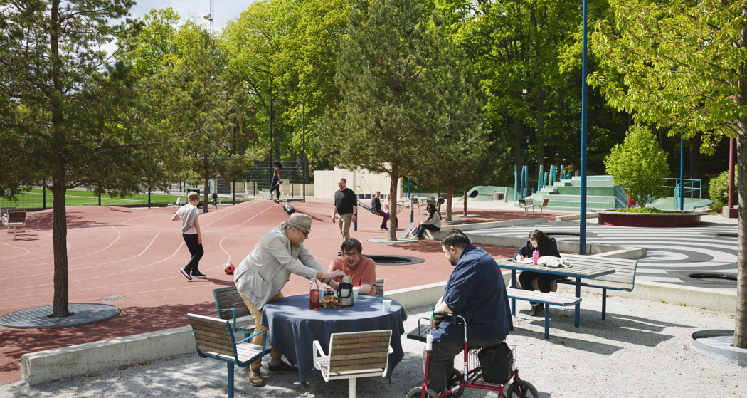 Foto av en grupp människor som sitter runt ett bord i en park.