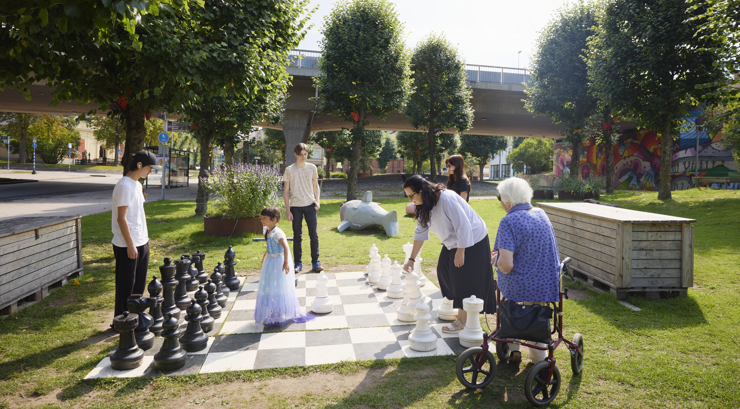 Foto av flera personer i olika åldrar som spelar trädgårds-schack i en allmän park.