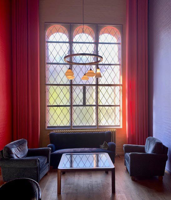 Foto på en soffgrupp med bord framför ett högt spröjsat fönster.